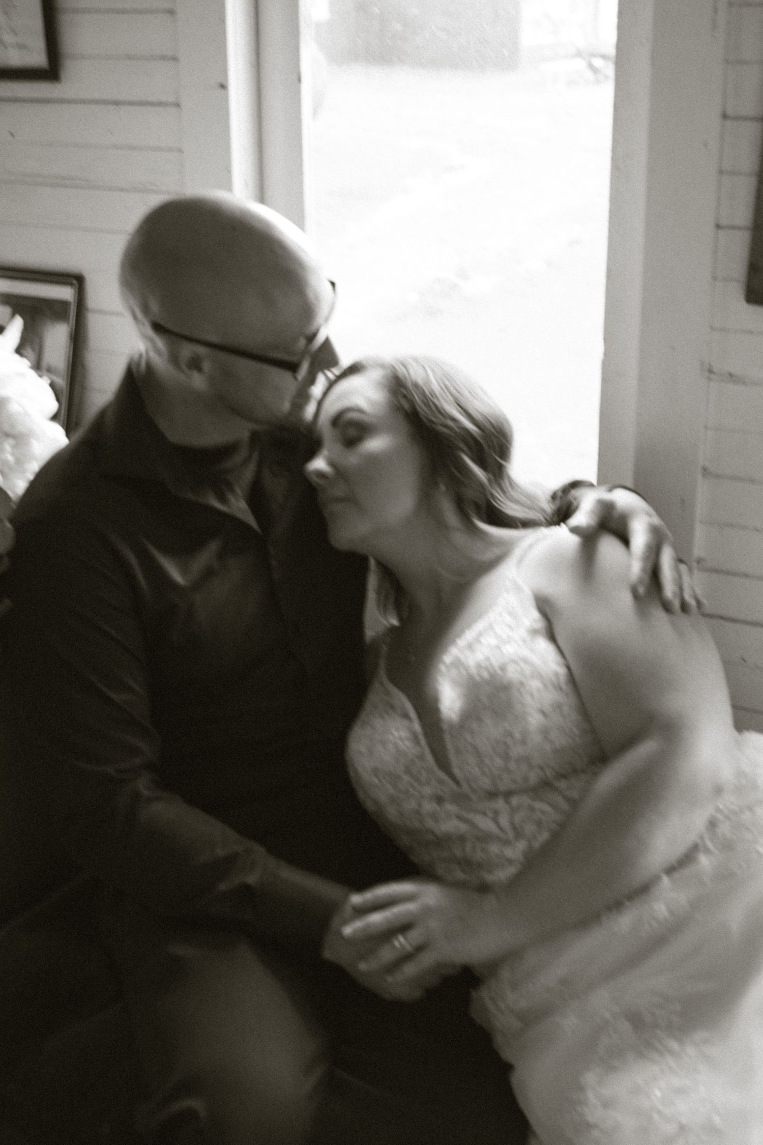 Black and white photo of a bride in lace gown and groom sharing a tender kiss at a wedding ceremony.