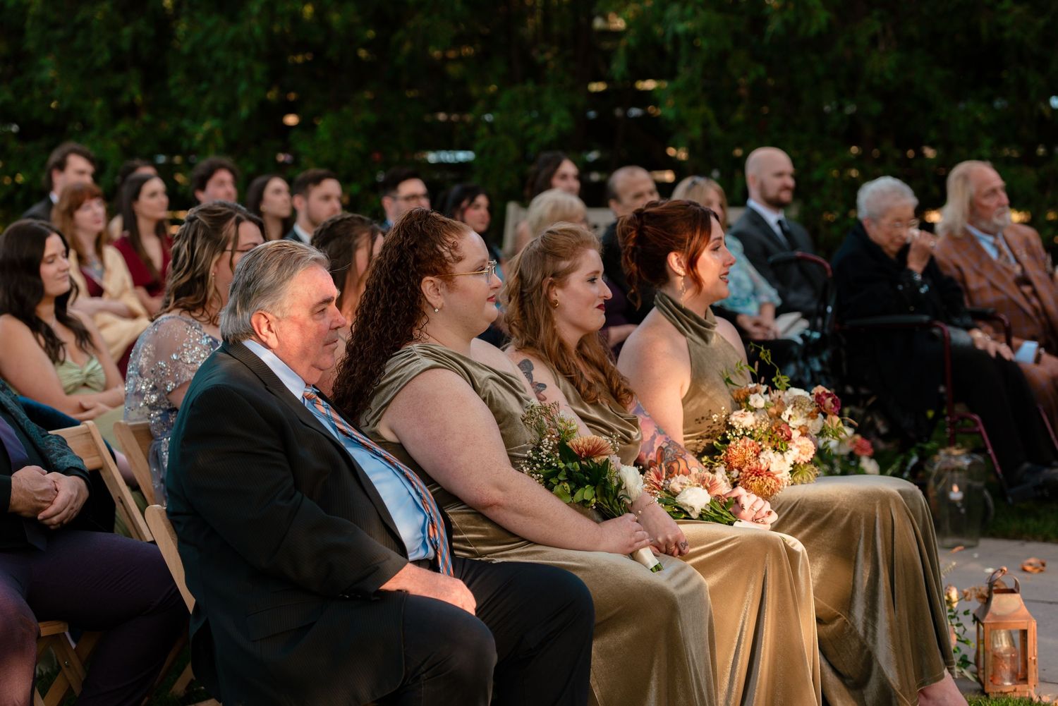 Guests seated outdoors at a wedding ceremony, wearing formal attire, in floral setting at Terrain at Styers Wedding Venue