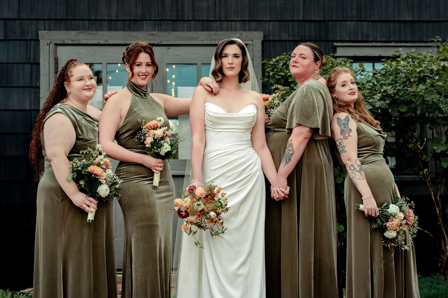 Bride in white gown with four bridesmaids in olive green dresses holding bouquets outside the Mushroom House at Terrain at Styers