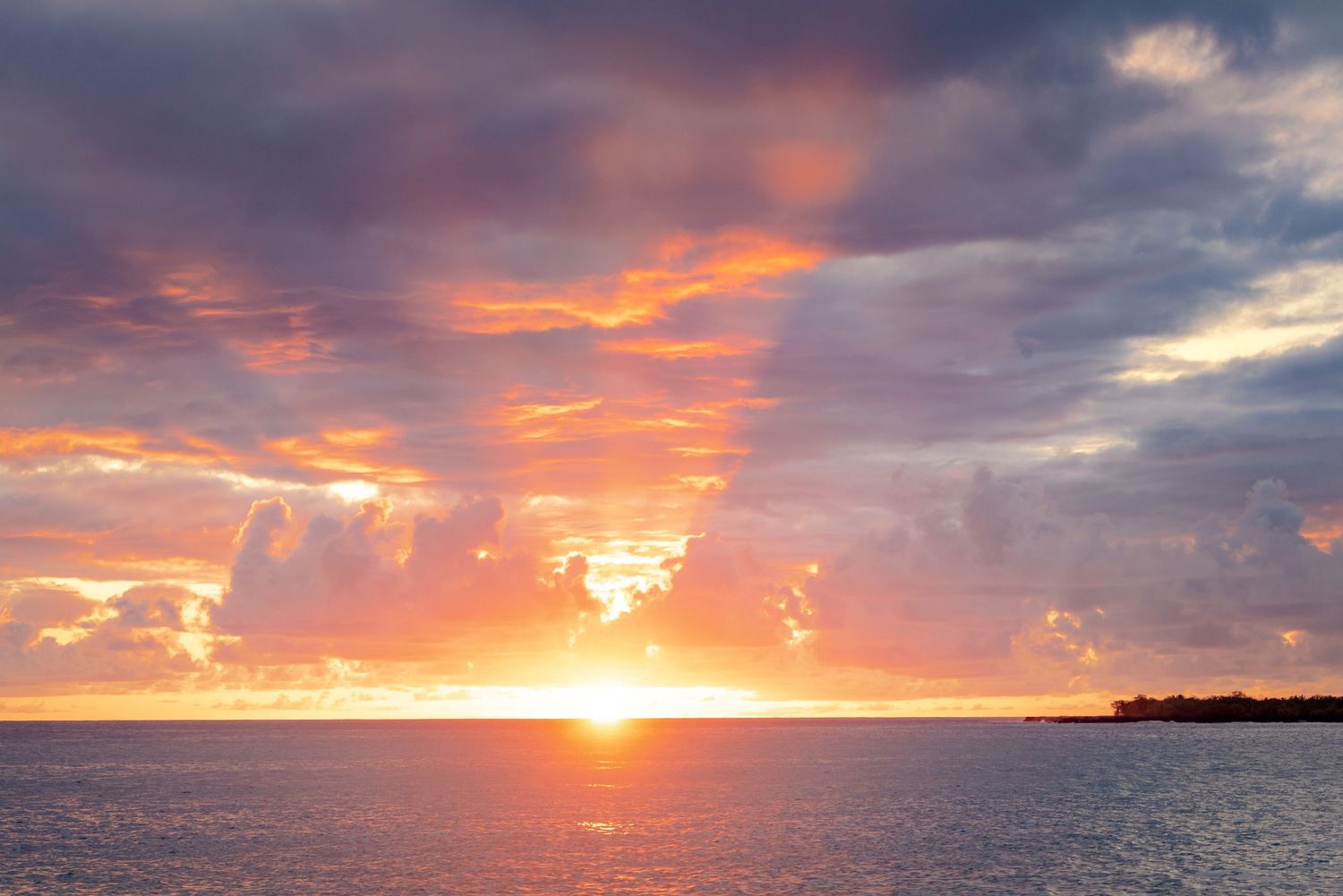 Stunning ocean sunset with vibrant orange and pink hues illuminating dramatic clouds over calm sea waters.