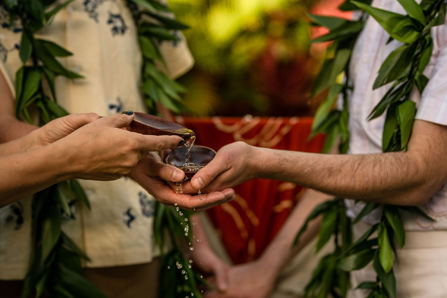 Couple exchanging rings during a tropical Hawaiian wedding ceremony with green leaf leis.