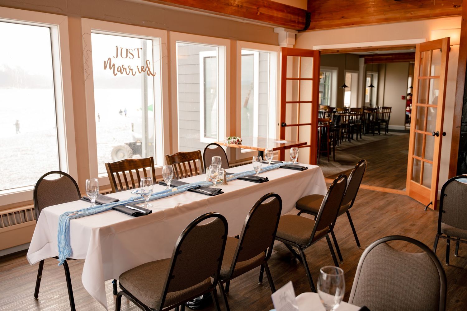 Elegant wedding reception dining room with white tablecloths, Just Married sign, and waterfront views through large windows at Lands End