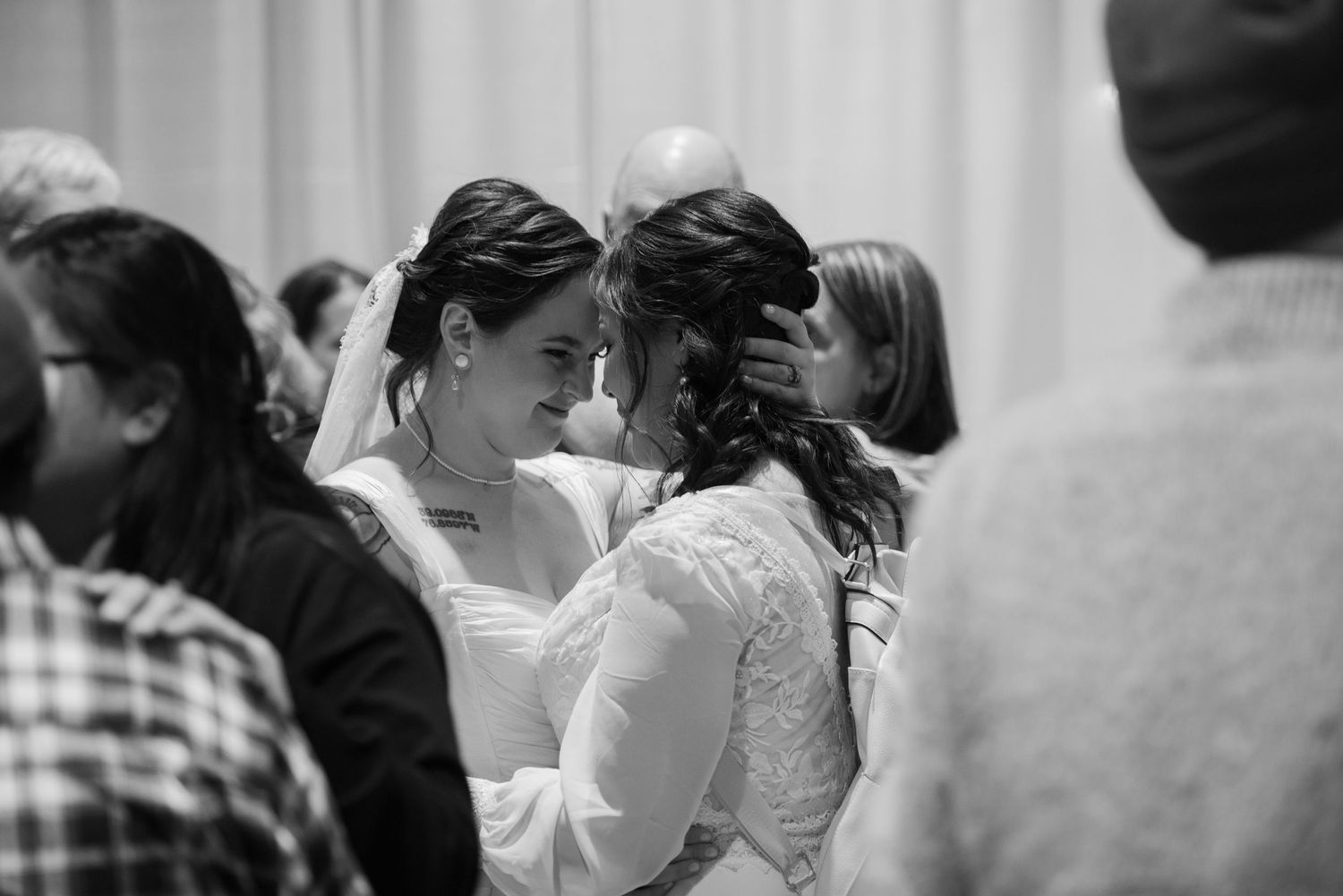 Two brides share an intimate moment touching foreheads at their wedding ceremony in black and white photo.
