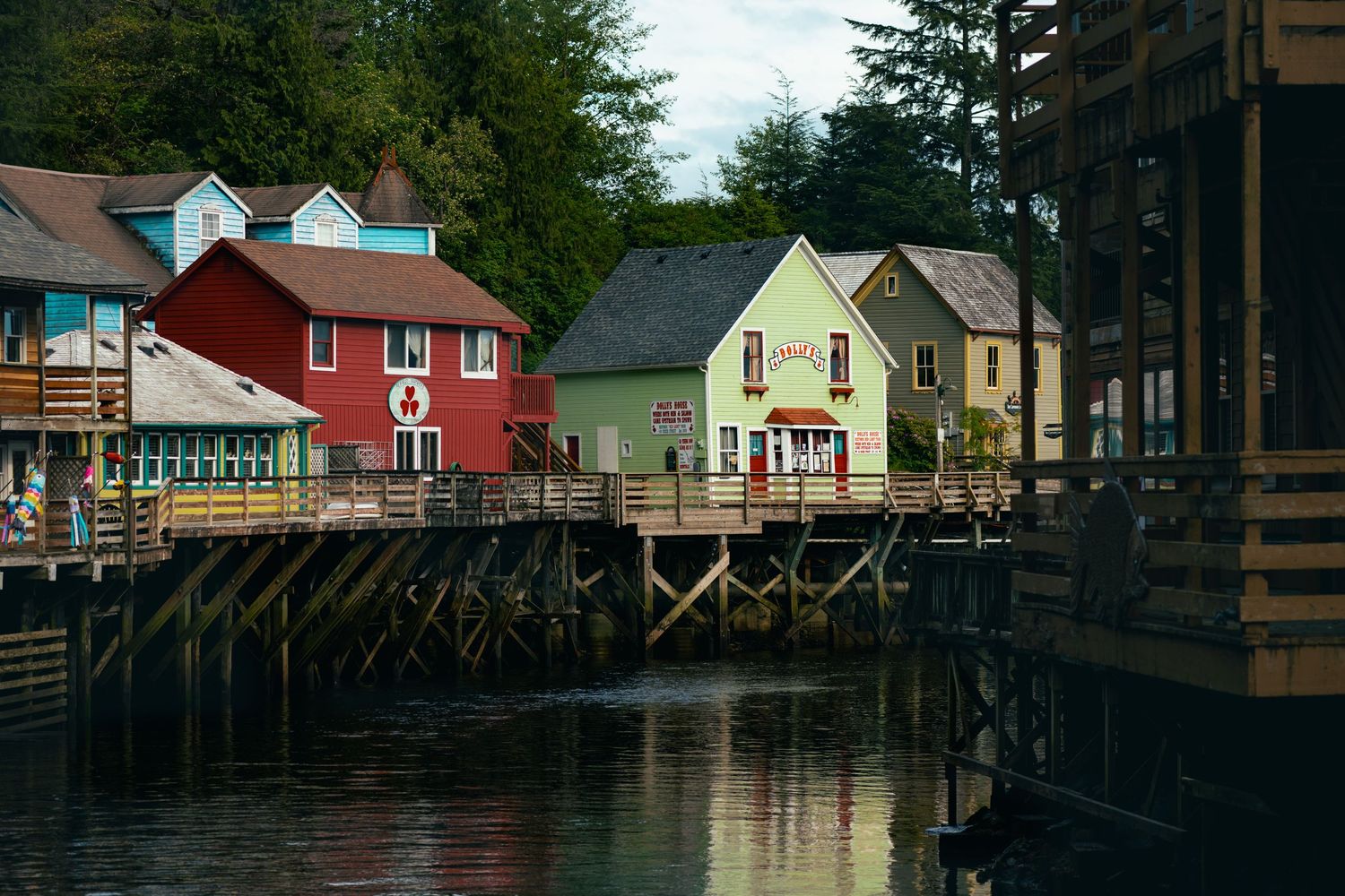Colorful waterfront buildings on wooden stilts reflect in calm waters in a charming Alaska harbor town.