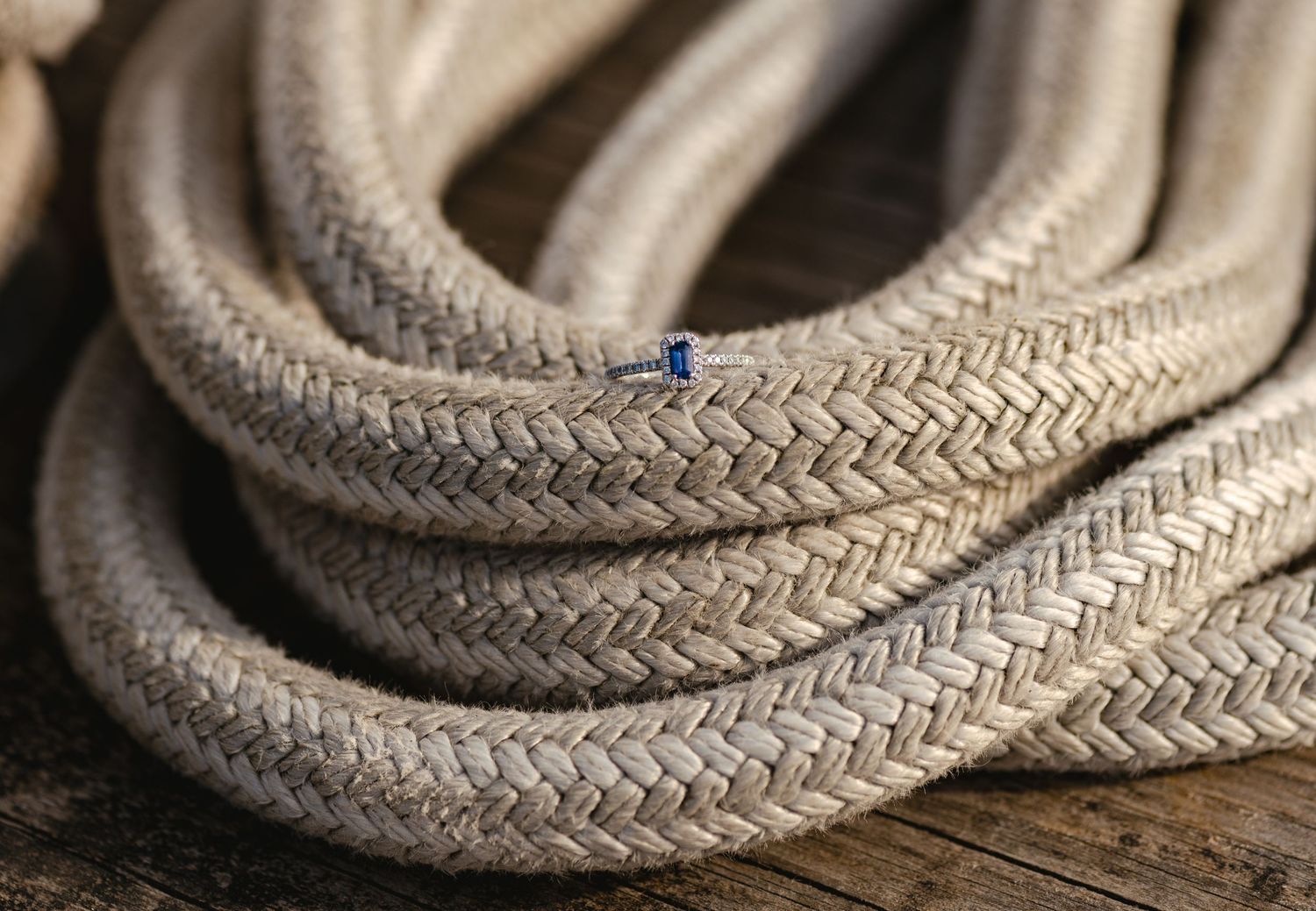Close-up of a coiled braided Ship rope with a blue thread marker resting on a rustic wooden surface.
