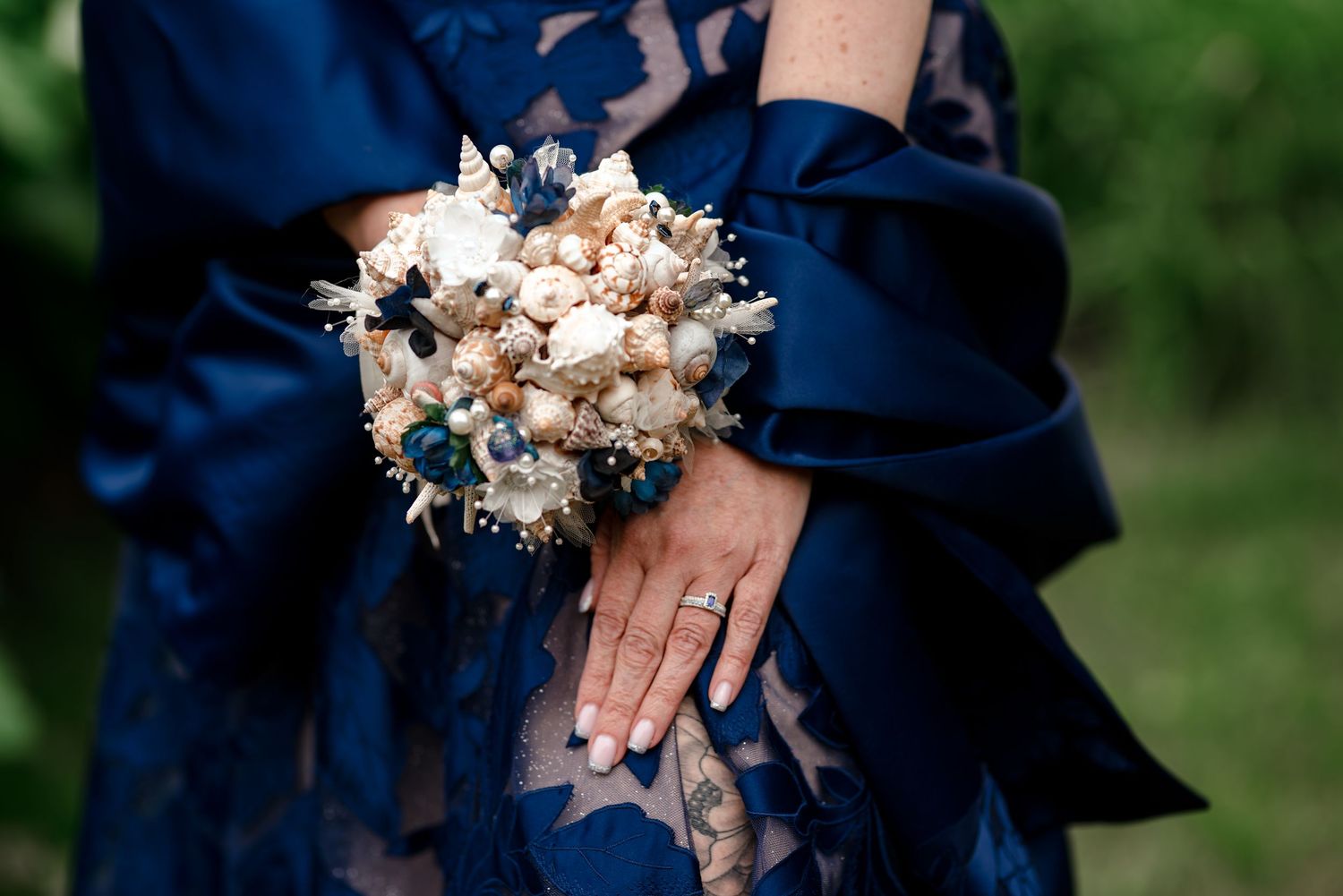 Bride in navy blue dress holding elegant wrist corsage with white and blue flowers, wearing diamond ring.