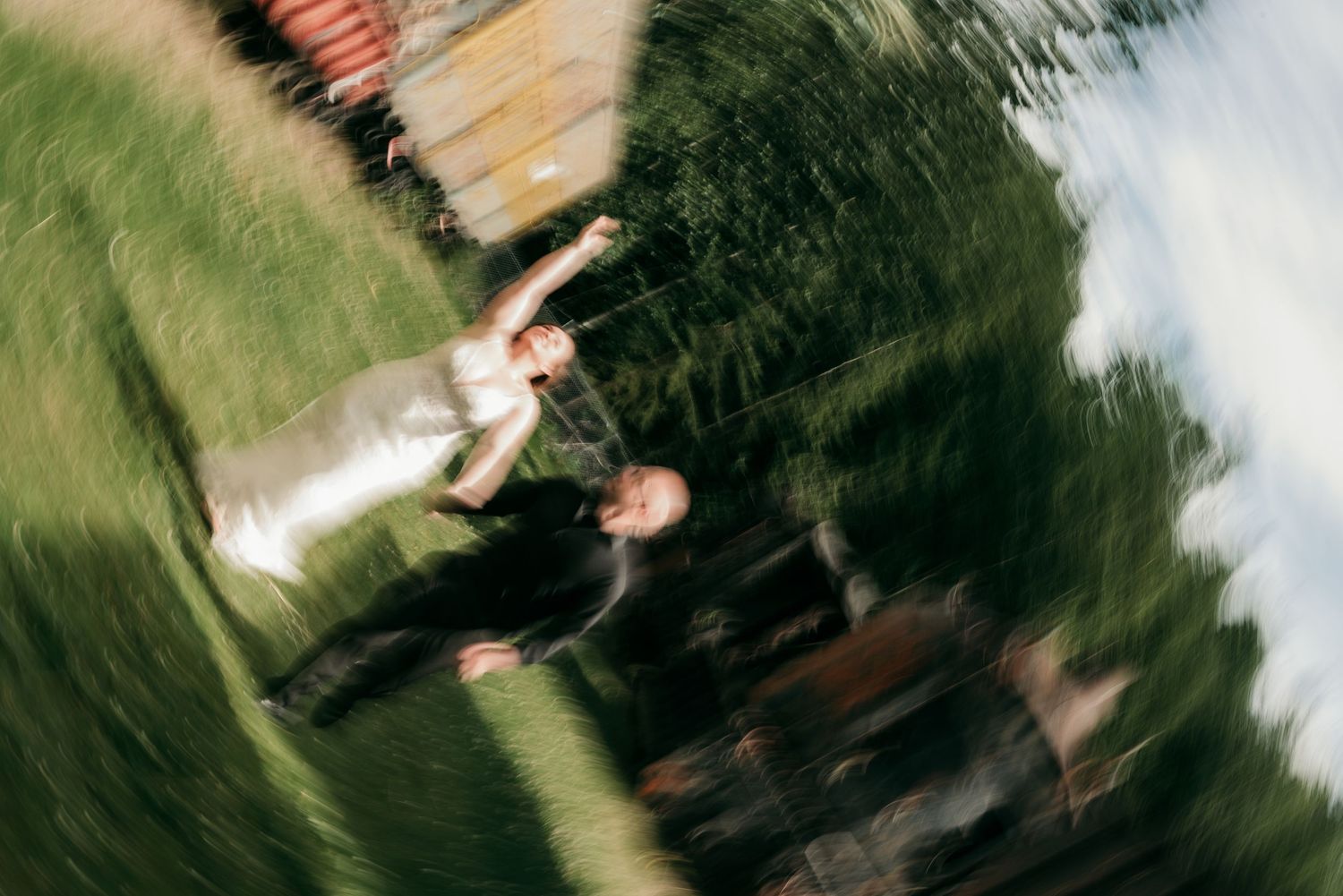 Wedding couple tossing bouquet in a blurred effect surrounded by green grass and rustic trains.