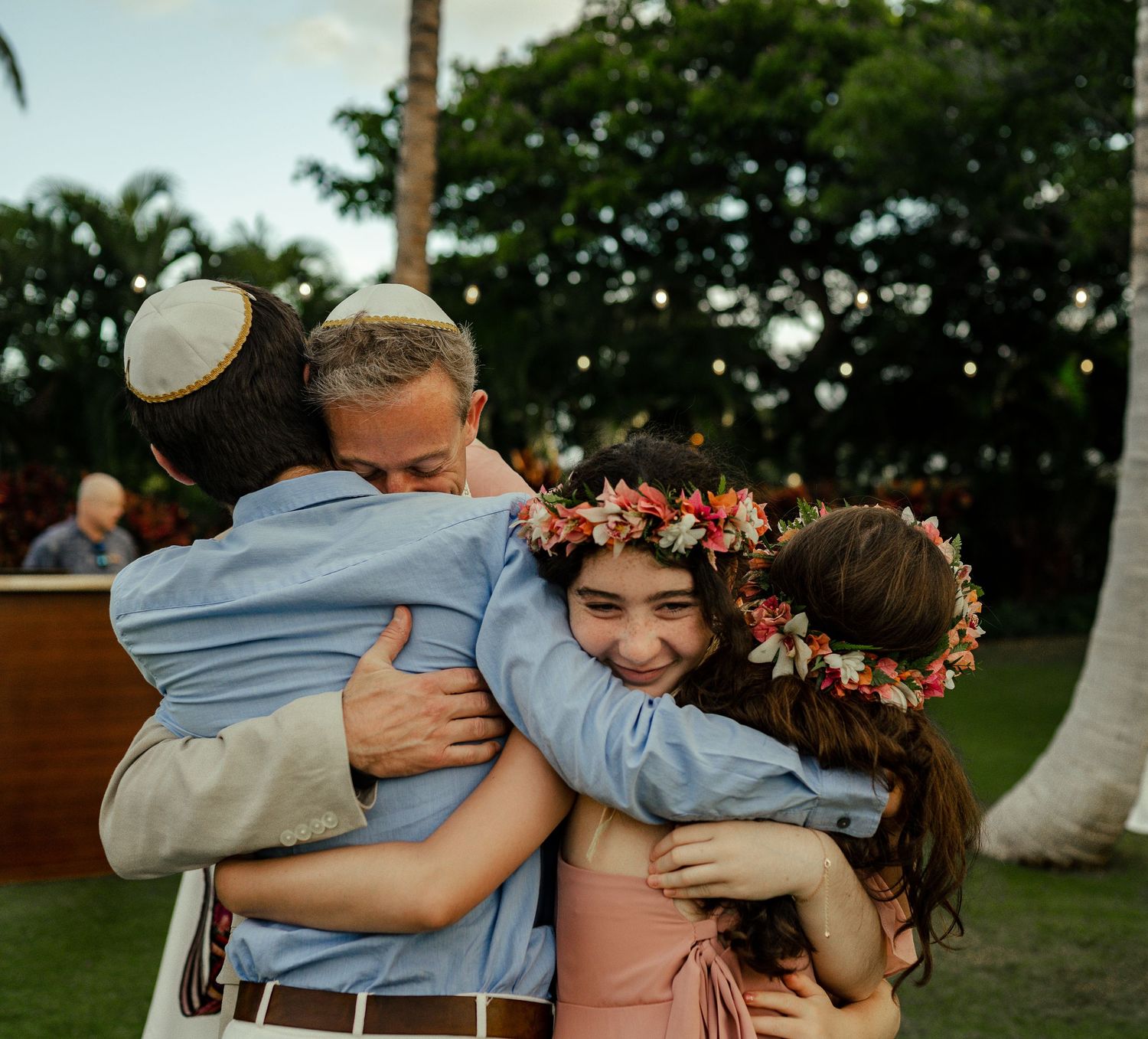 An emotional group hug captured during a sunny outdoor wedding celebration.