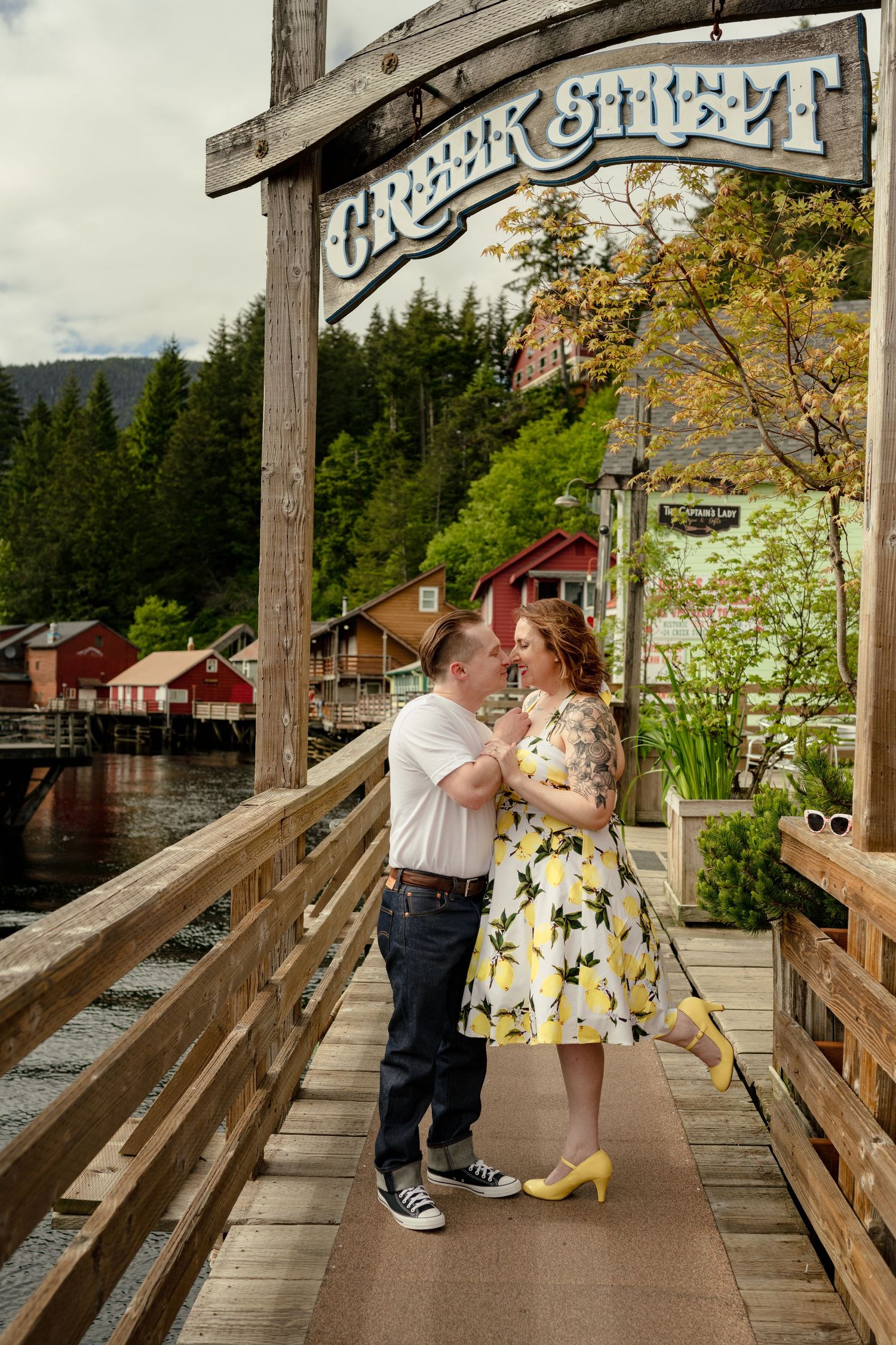 Couple sharing a romantic moment on Creek Street boardwalk in Ketchikan, Alaska, with colorful waterfront buildings behind them.