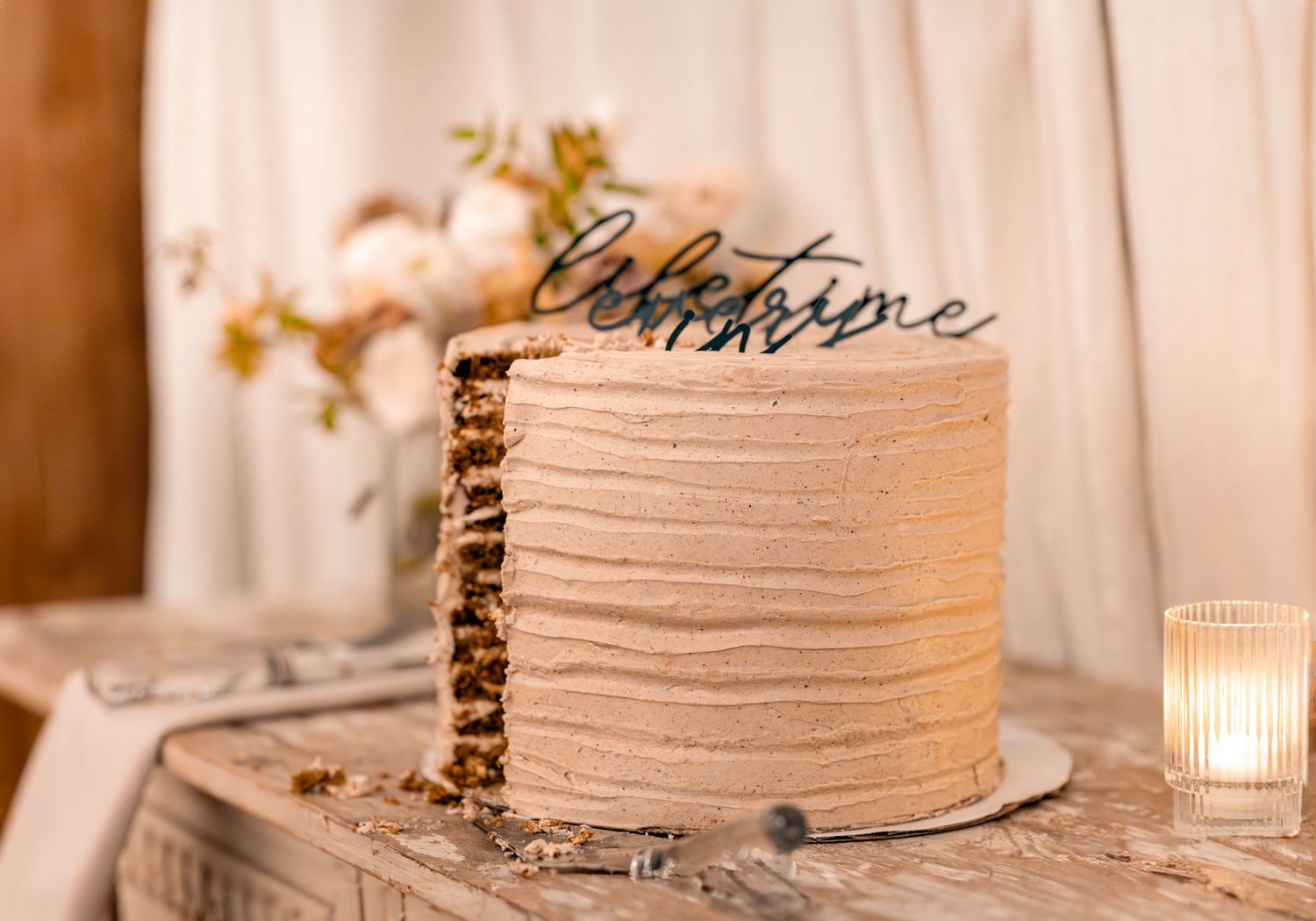 Elegant wedding cake with textured frosting and a cursive lifetime cake topper on a rustic wooden table.