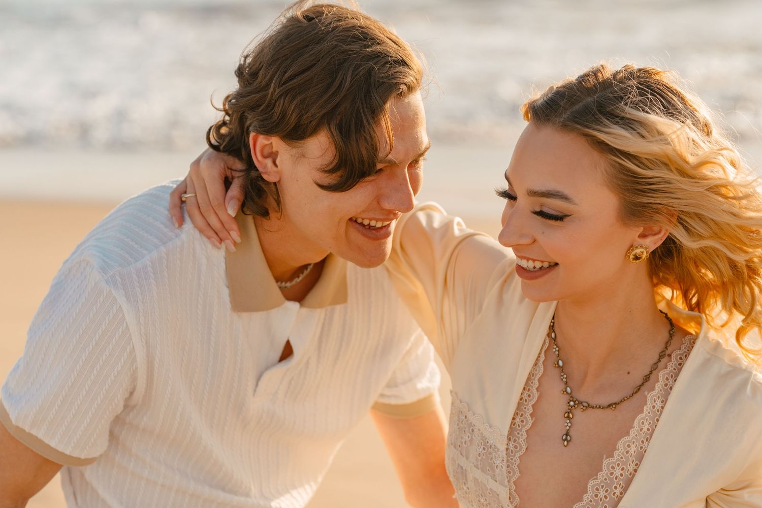 Close up of couple laughing together on beach at golden hour.