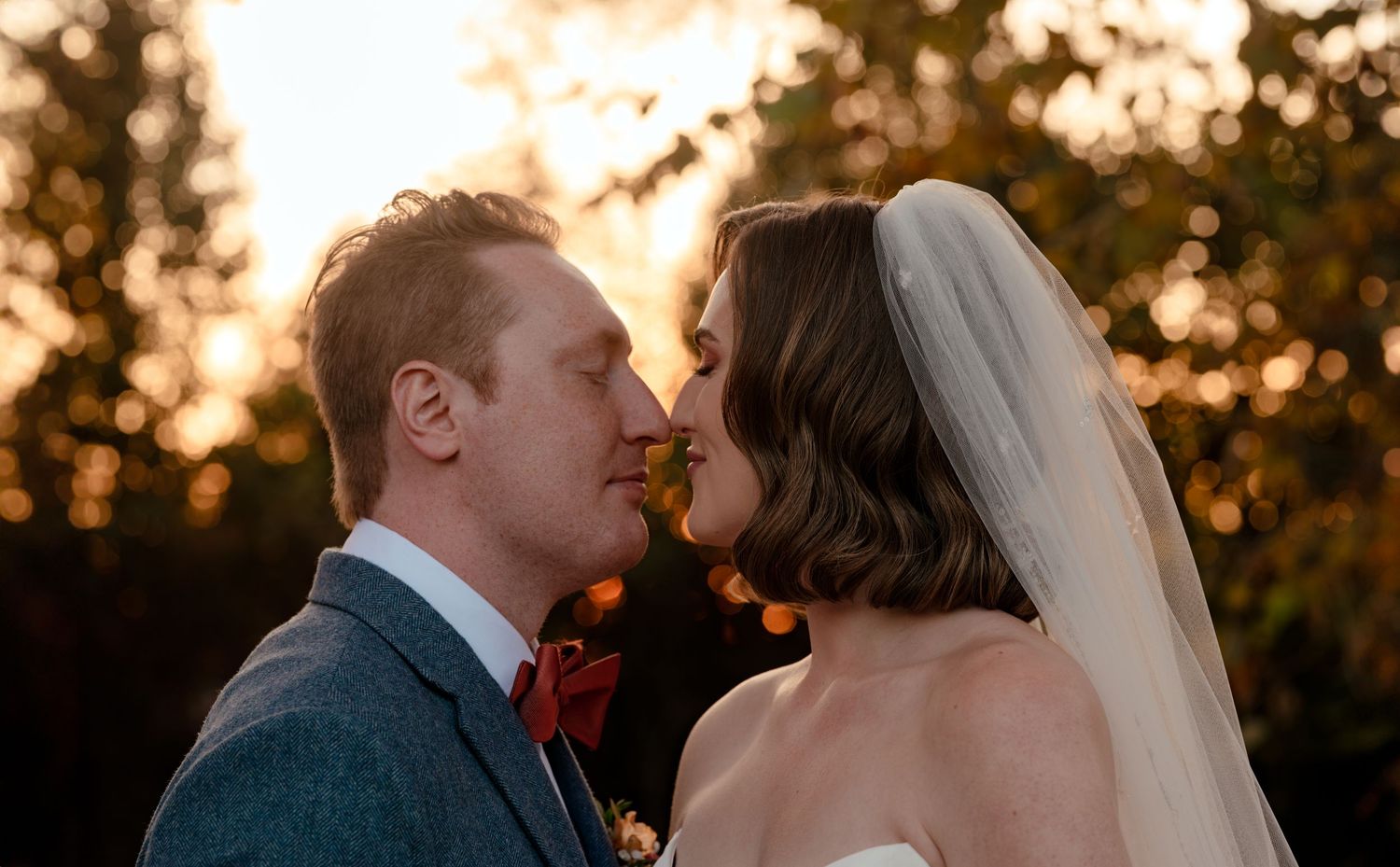 Bride and groom sharing a romantic moment at golden hour, with the bride wearing a veil outdoors.