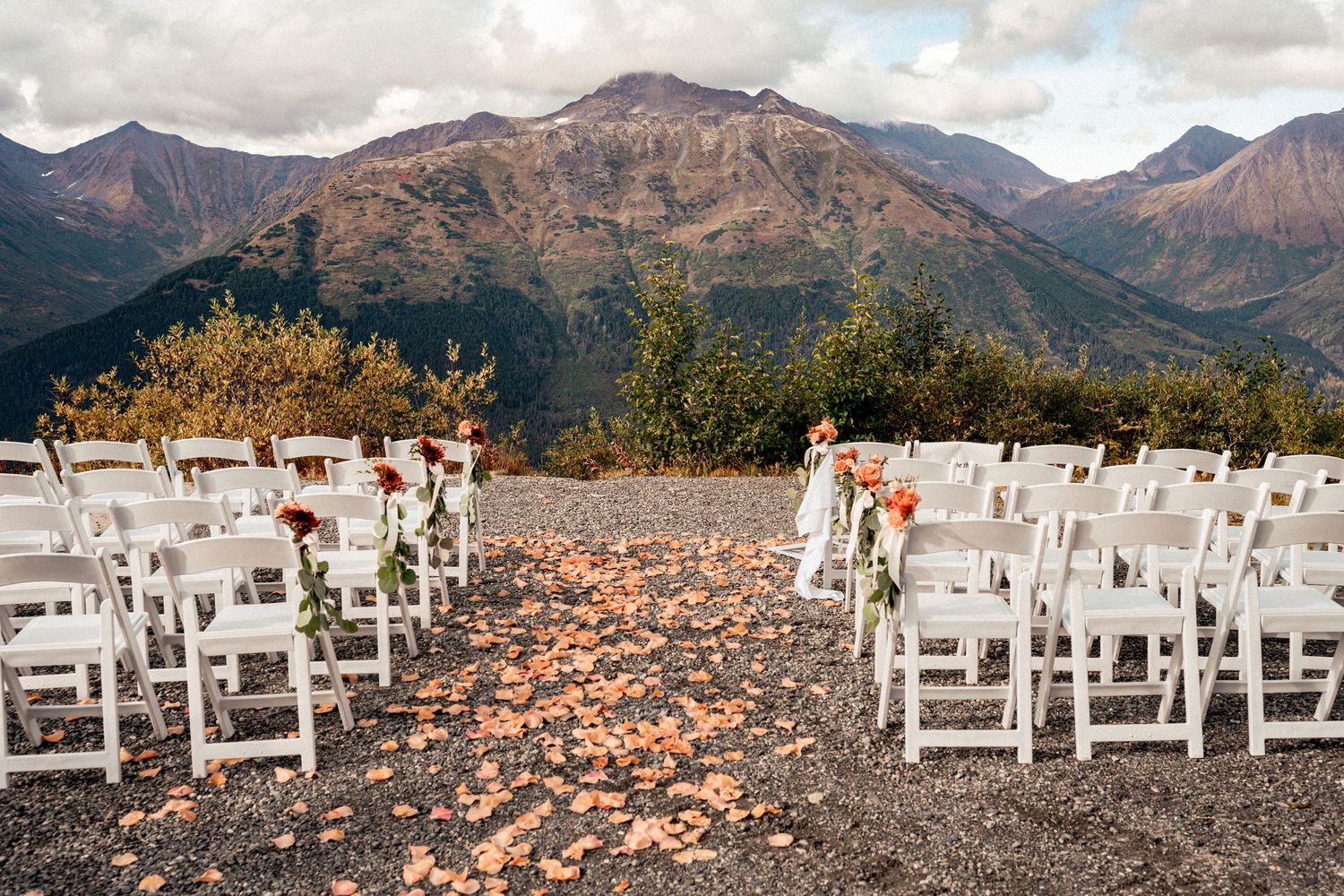 Outdoor mountain wedding ceremony setup with white chairs and floral arrangements against a stunning alpine backdrop.