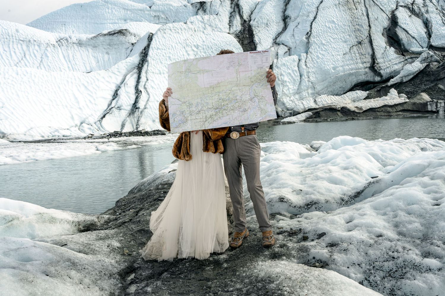 Couple in wedding attire holding a map in front of a glacier landscape in Iceland.