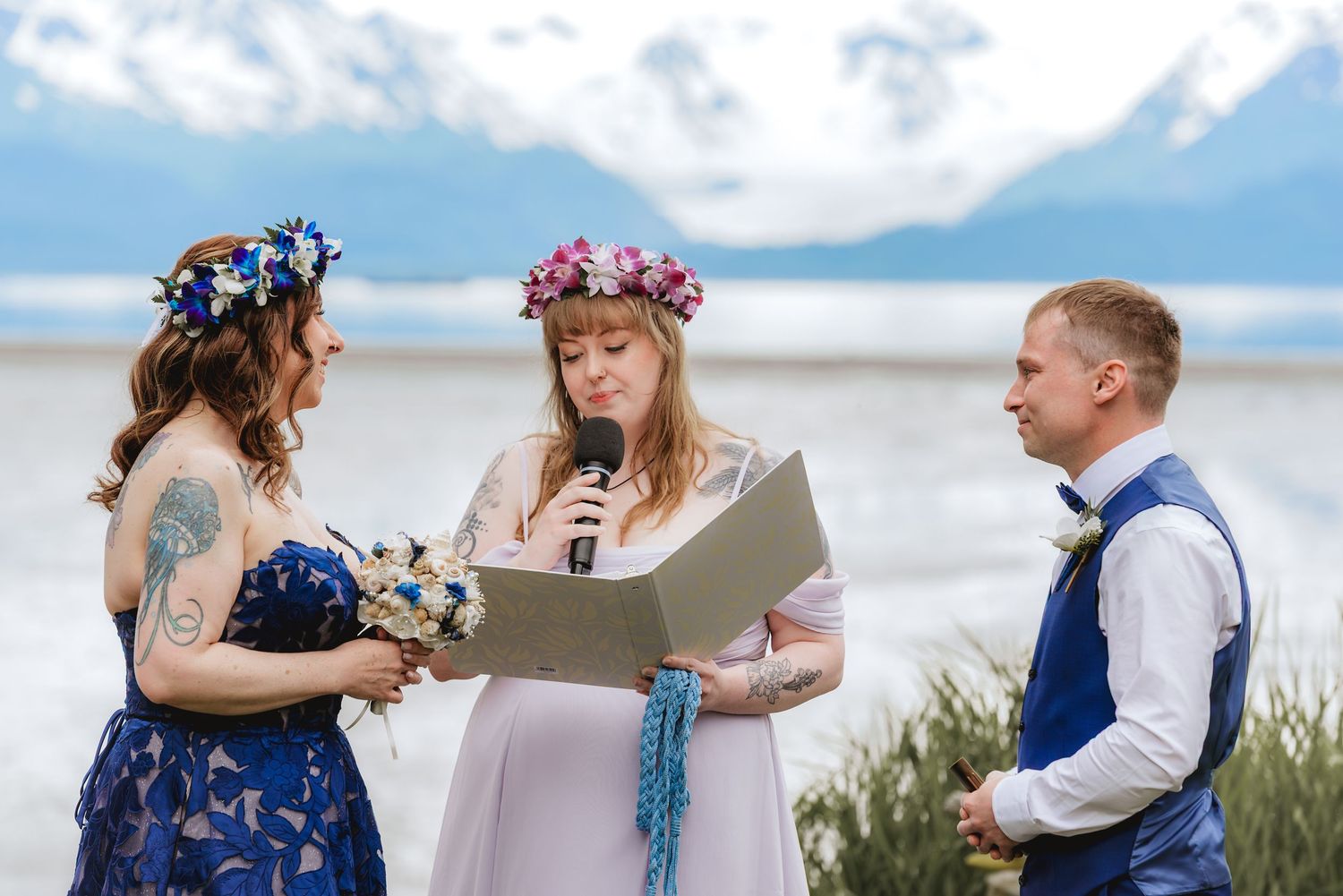 Outdoor elopement in Homer Alaska with Bride in blue gown and daughter officiating. Mountains in the background on a sunny day