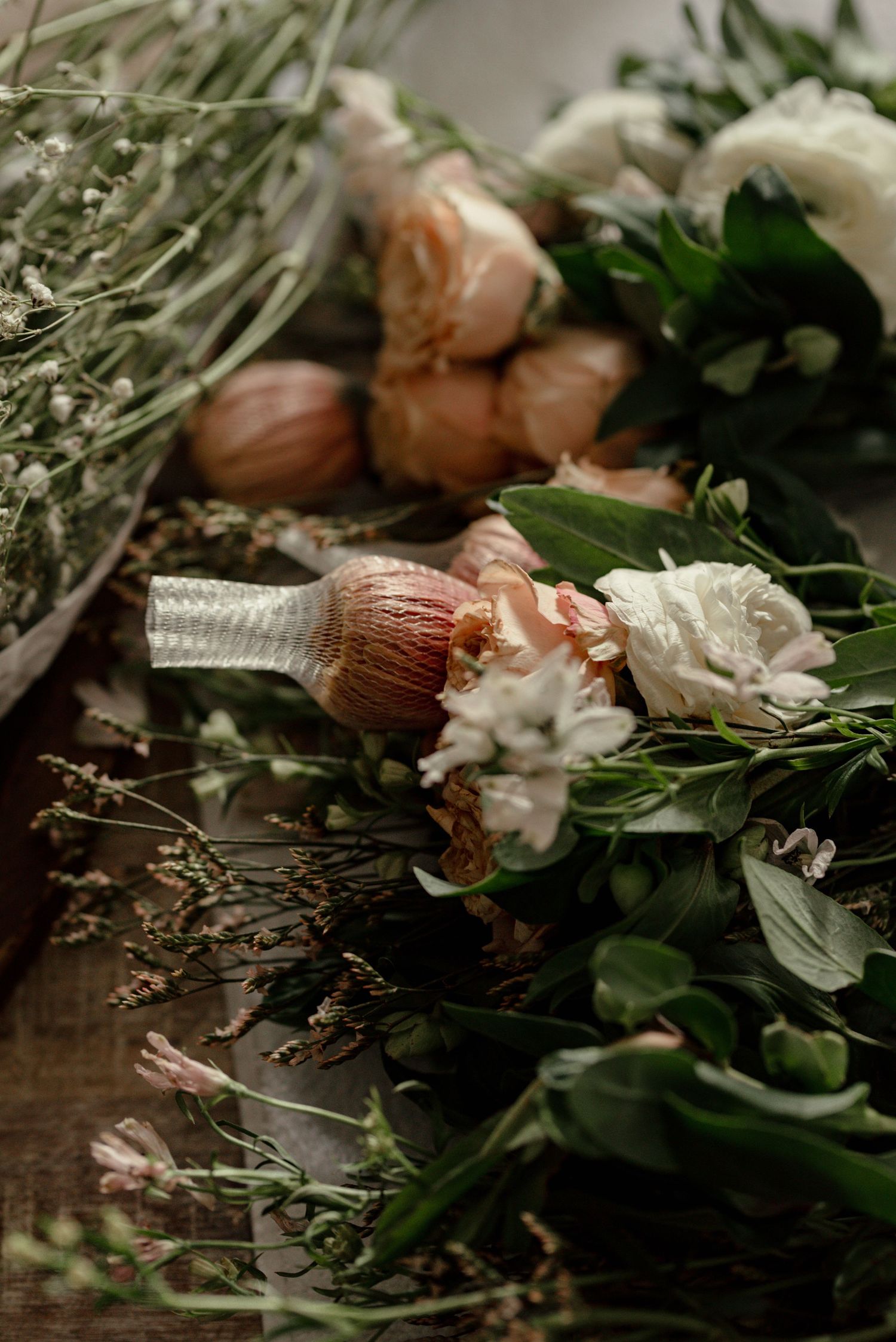 Flat lay of fresh white and pink roses, dried wildflowers, and lush green foliage arranged on a rustic wooden surface.