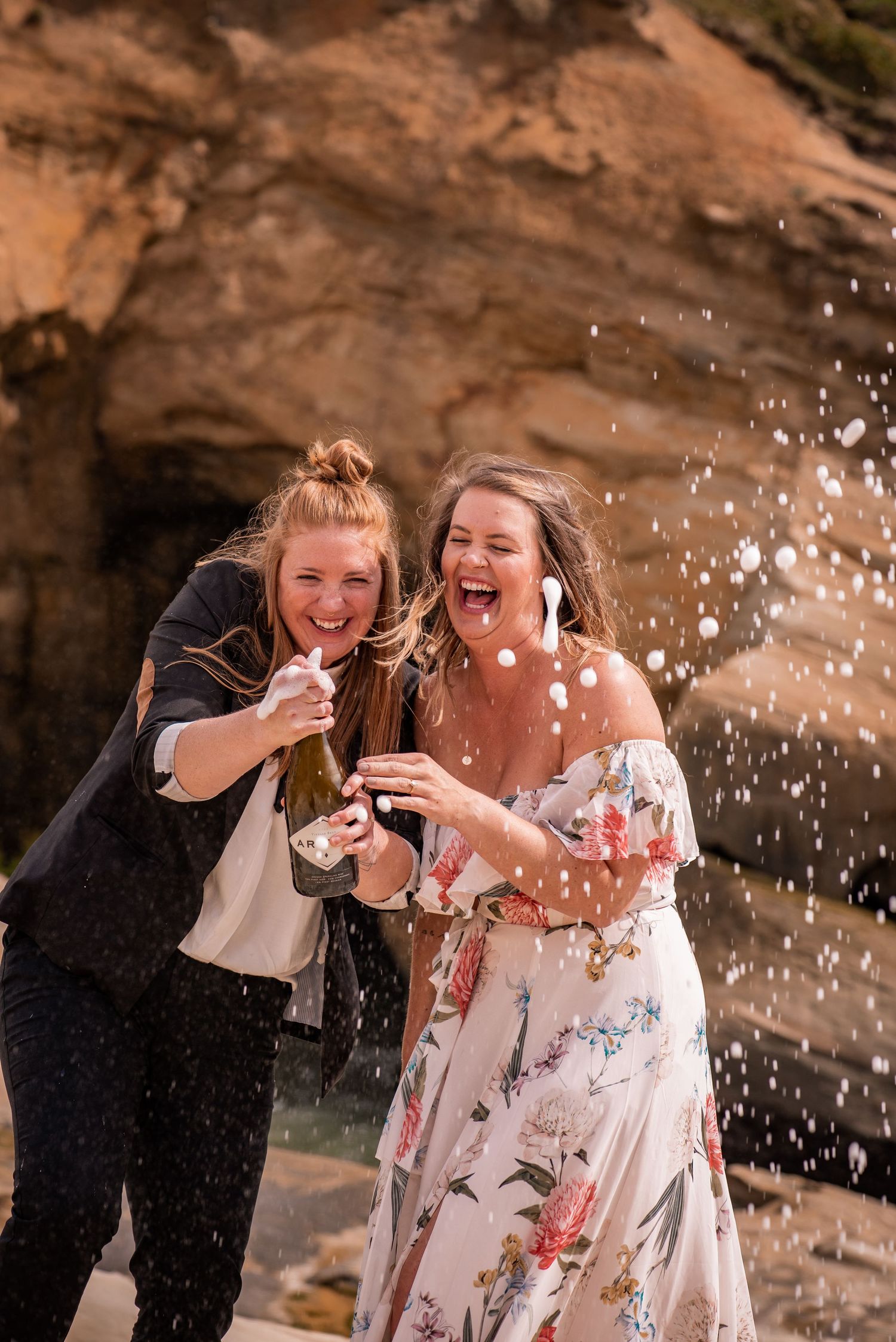 Two friends share joyful laughter while playing with water splashes against a rocky backdrop.