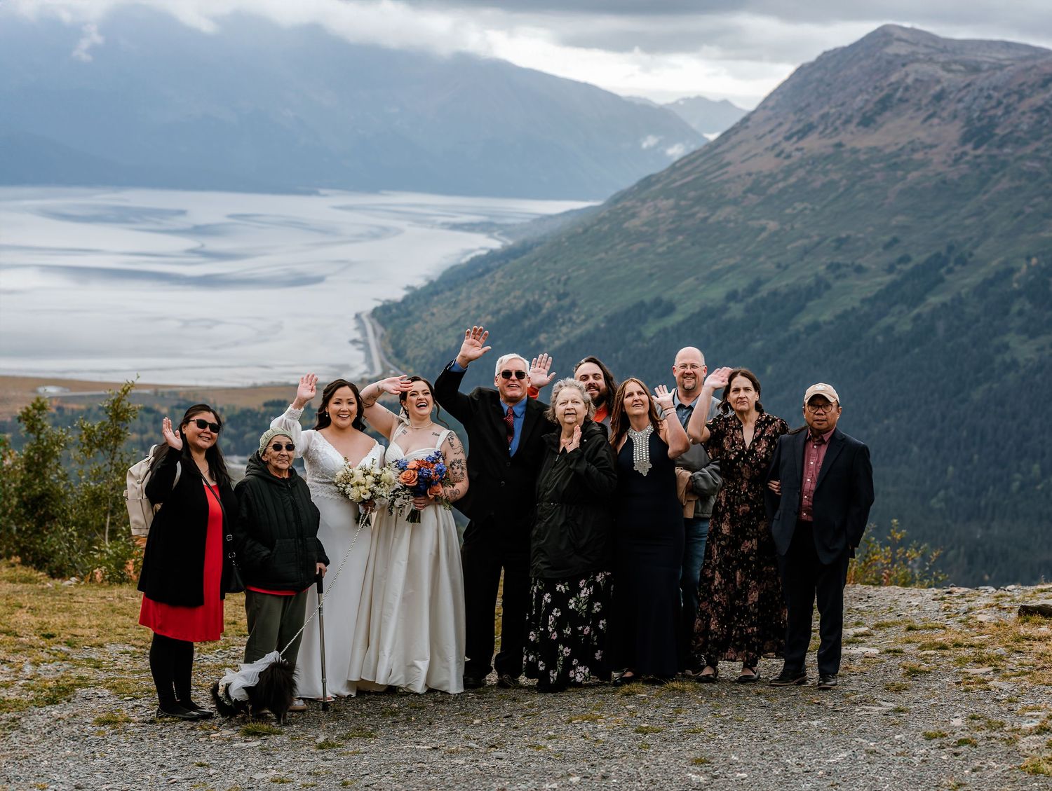 Wedding party celebrating outdoors on a mountain overlook with glacier and valley views in Alaska.