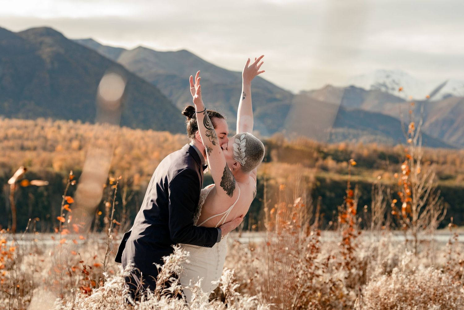 A couple dips dramatically while dancing in a field with mountain peaks in the background in Alaska.