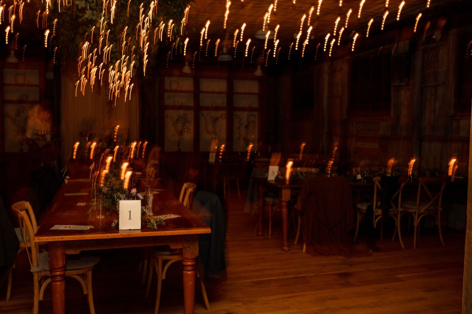 Candlelit restaurant dining room with wooden tables and chairs, warm amber glow reflecting in a long exposure photograph.