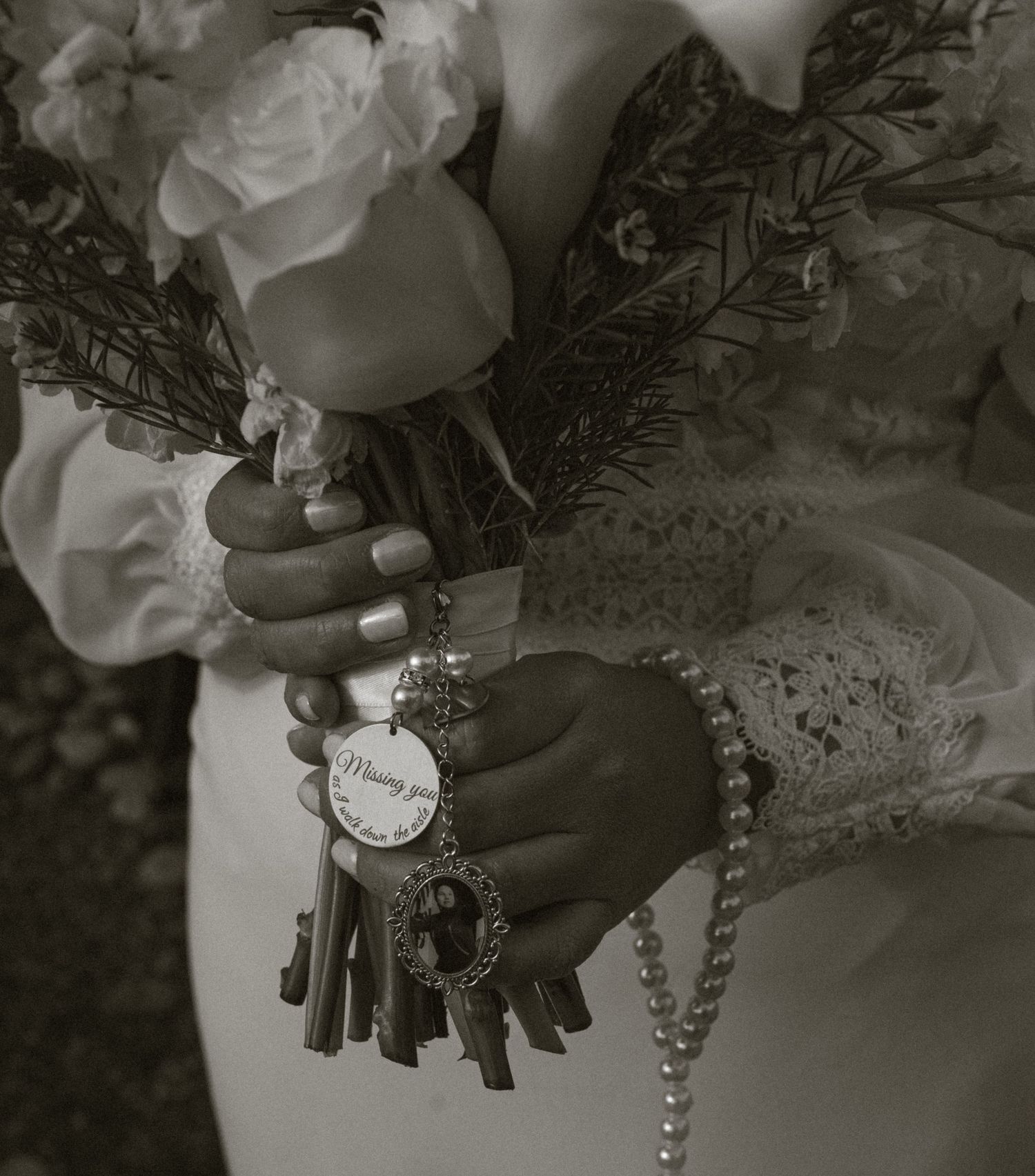 Bride holding white rose bouquet with memorial charm and pearl bracelet in black and white wedding photo.