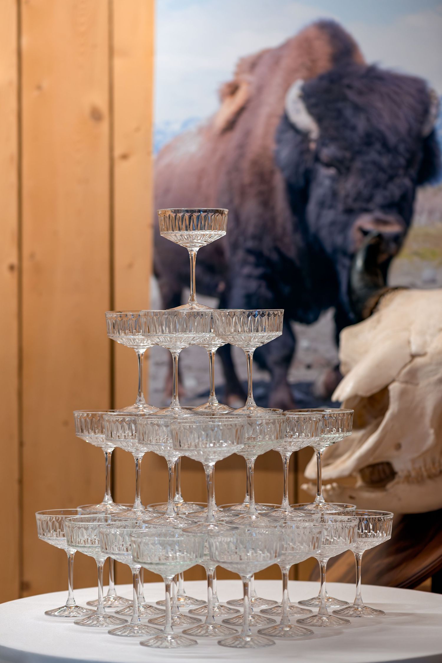 Crystal champagne tower pyramid on white table with bison photo backdrop at elegant event.