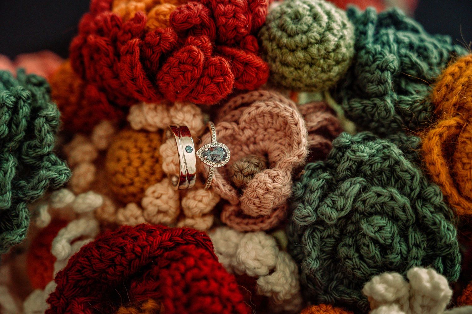 Colorful crocheted flower bouquet in red, green, teal, and orange yarn with a silver ring nestled among the blooms.