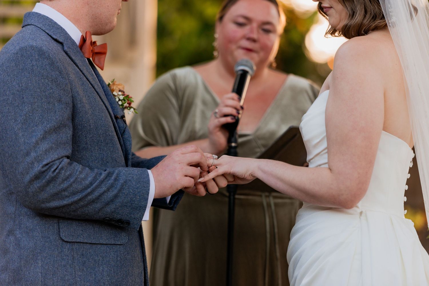 Groom places wedding ring on bride's finger during outdoor ceremony as they exchange their vows.