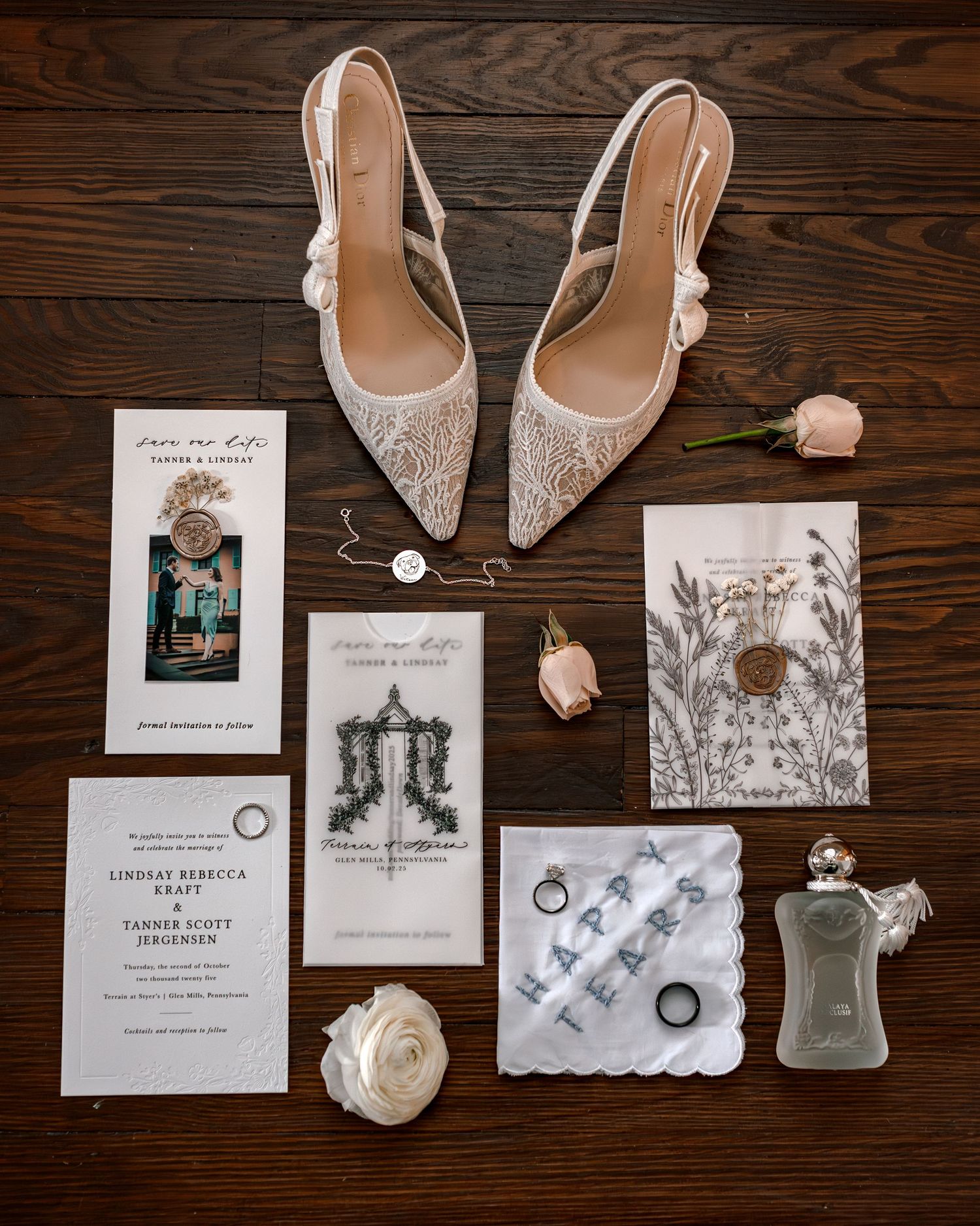 Elegant bridal flat lay featuring Gucci lace heels, wedding invitations, rings, perfume, roses, and accessories on dark wood.