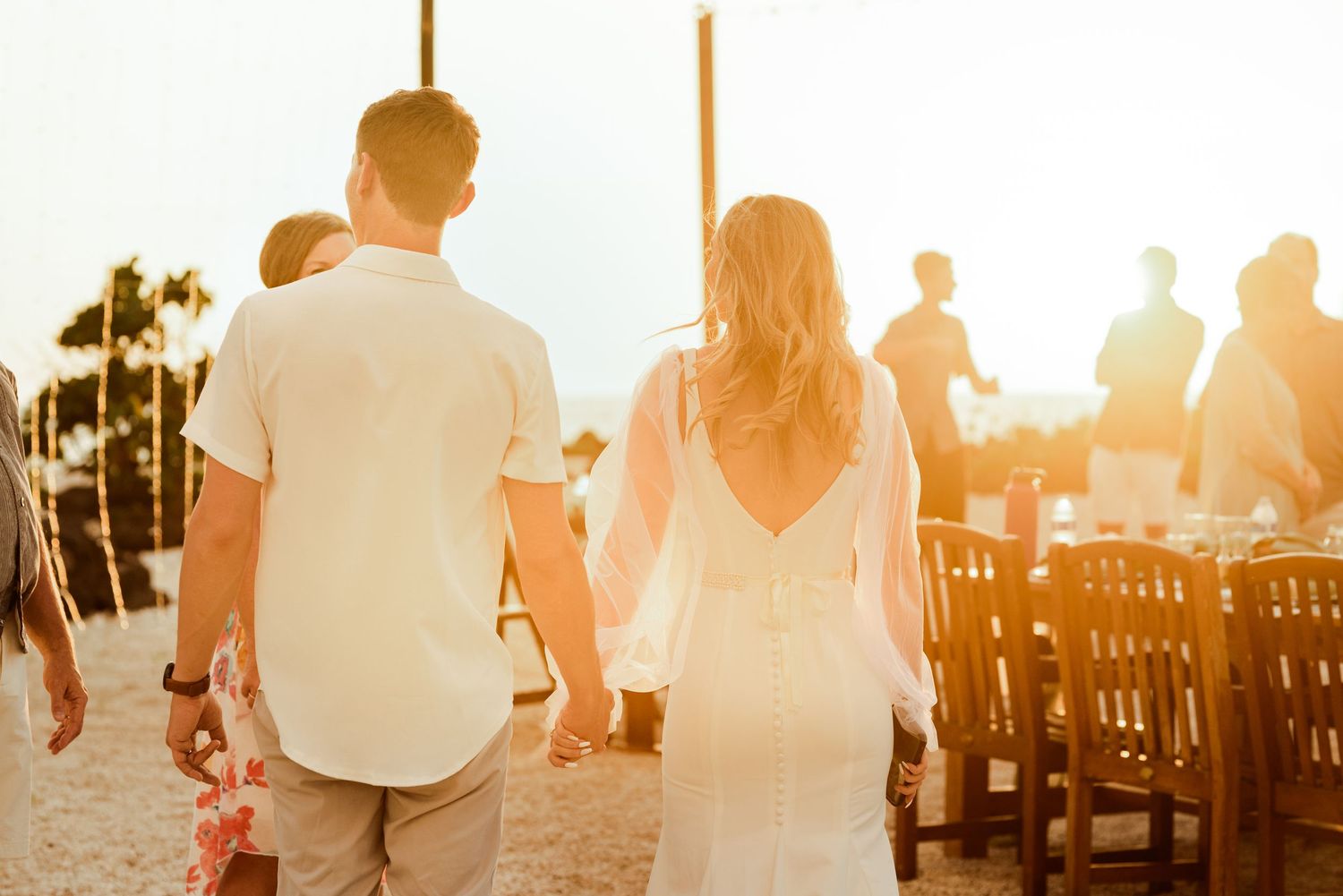 Couple walking hand in hand during golden hour sunset at an outdoor wedding reception in Kona, Hawaii.