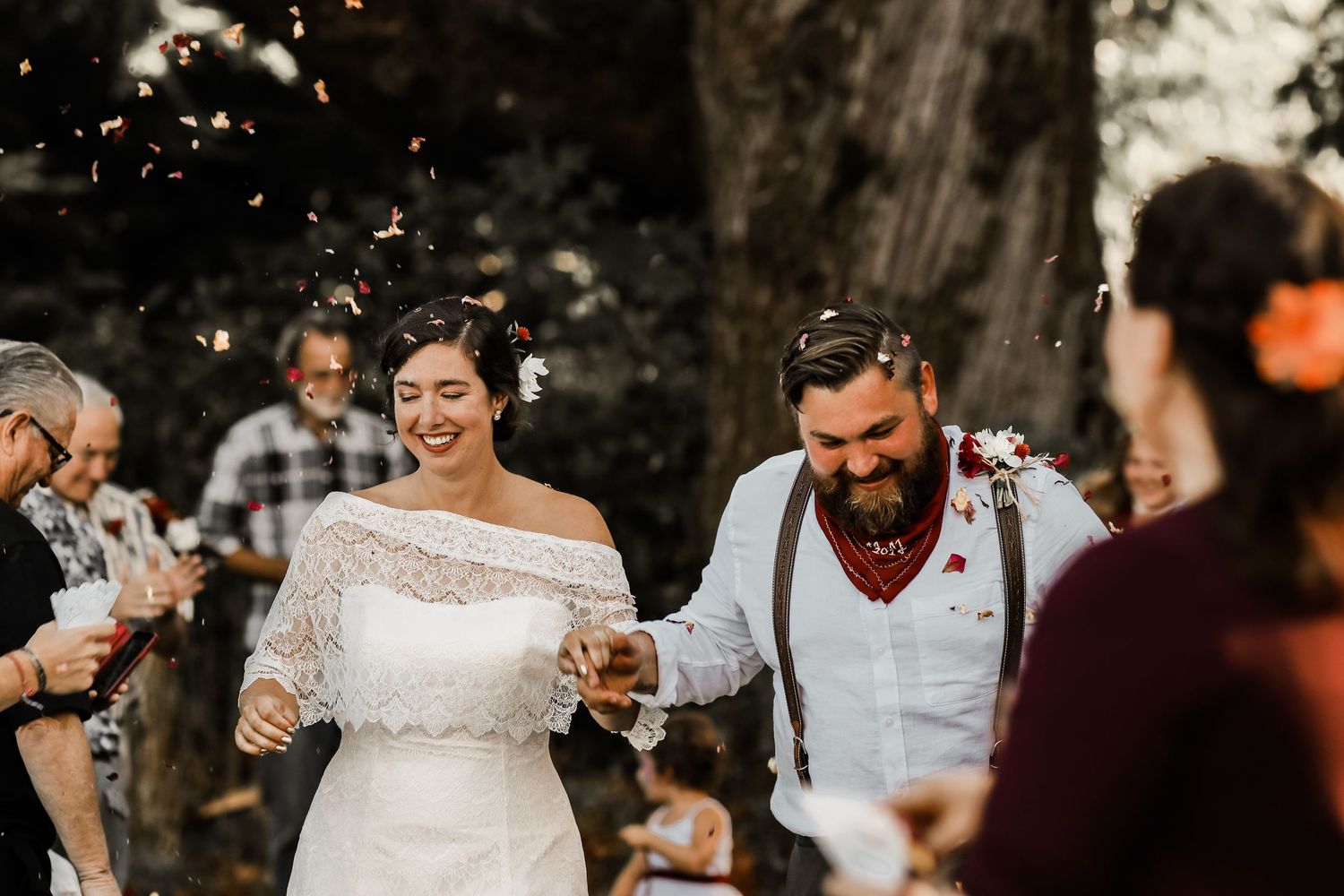 Wedding celebration with guests throwing confetti in outdoor setting.