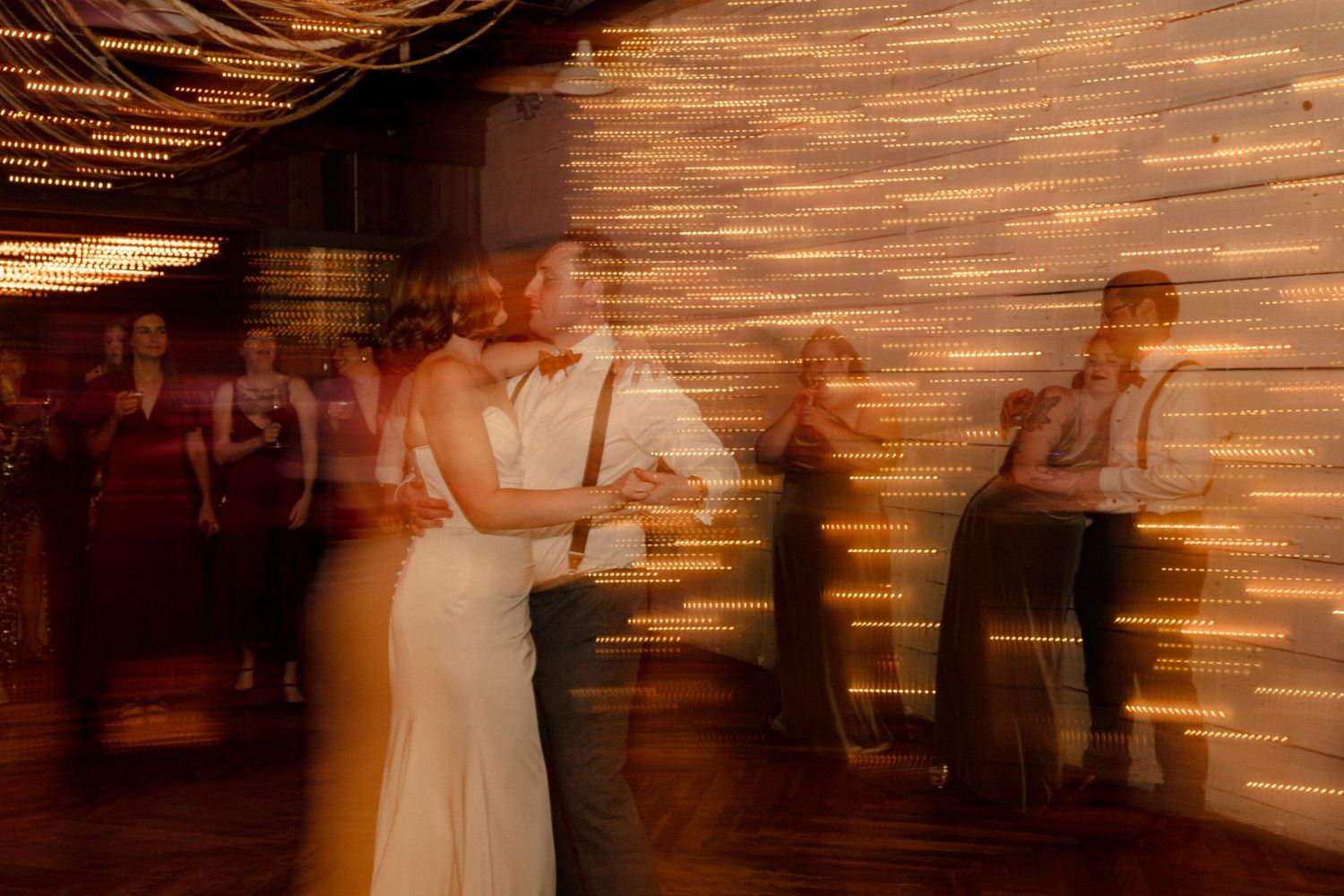 A sequence of motion blur images showing a person in a white dress dancing at a wedding reception.