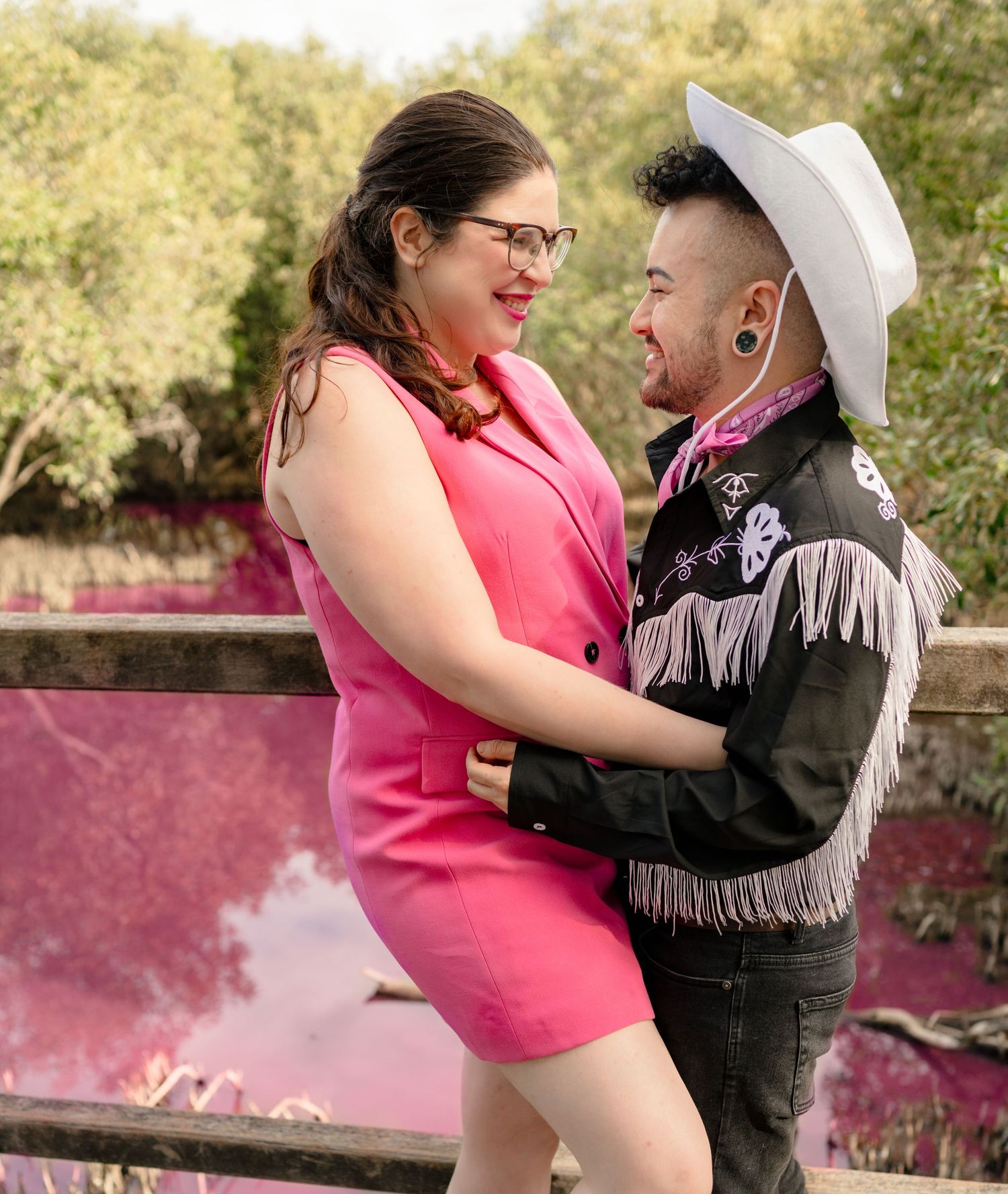 Couple in pink and black fringe jacket embracing on a bridge, smiling at each other outdoors.