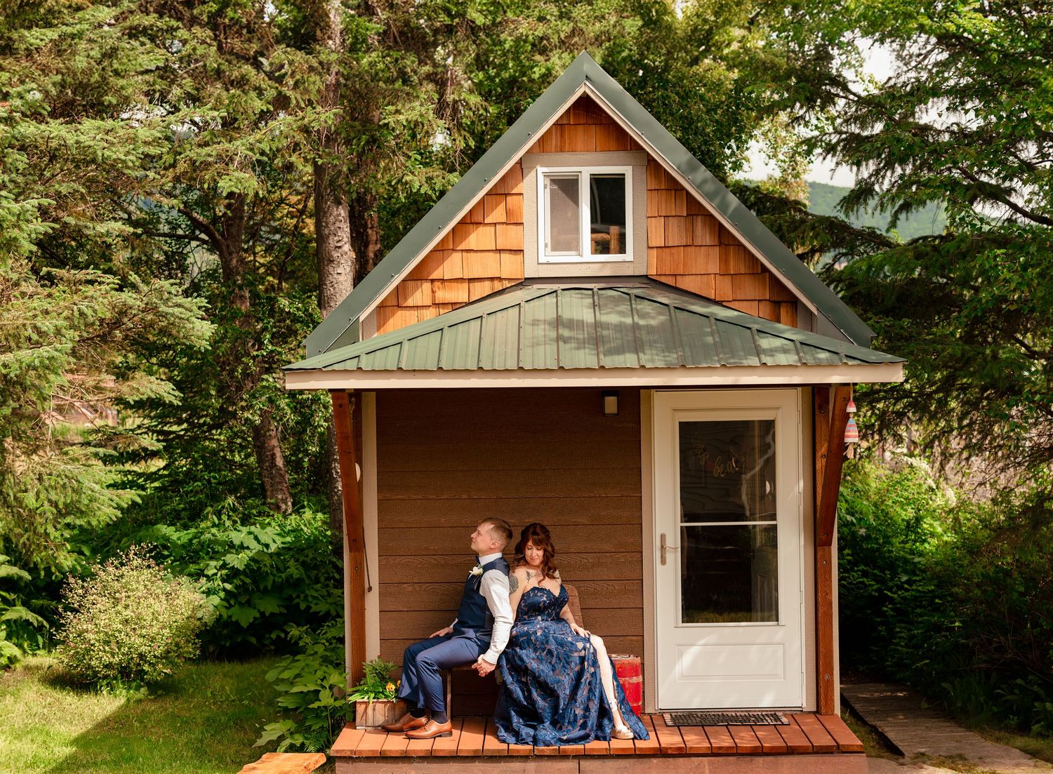 Wedding couple Couple sitting on porch of charming small cedar cabin surrounded by lush green trees, sharing a first look