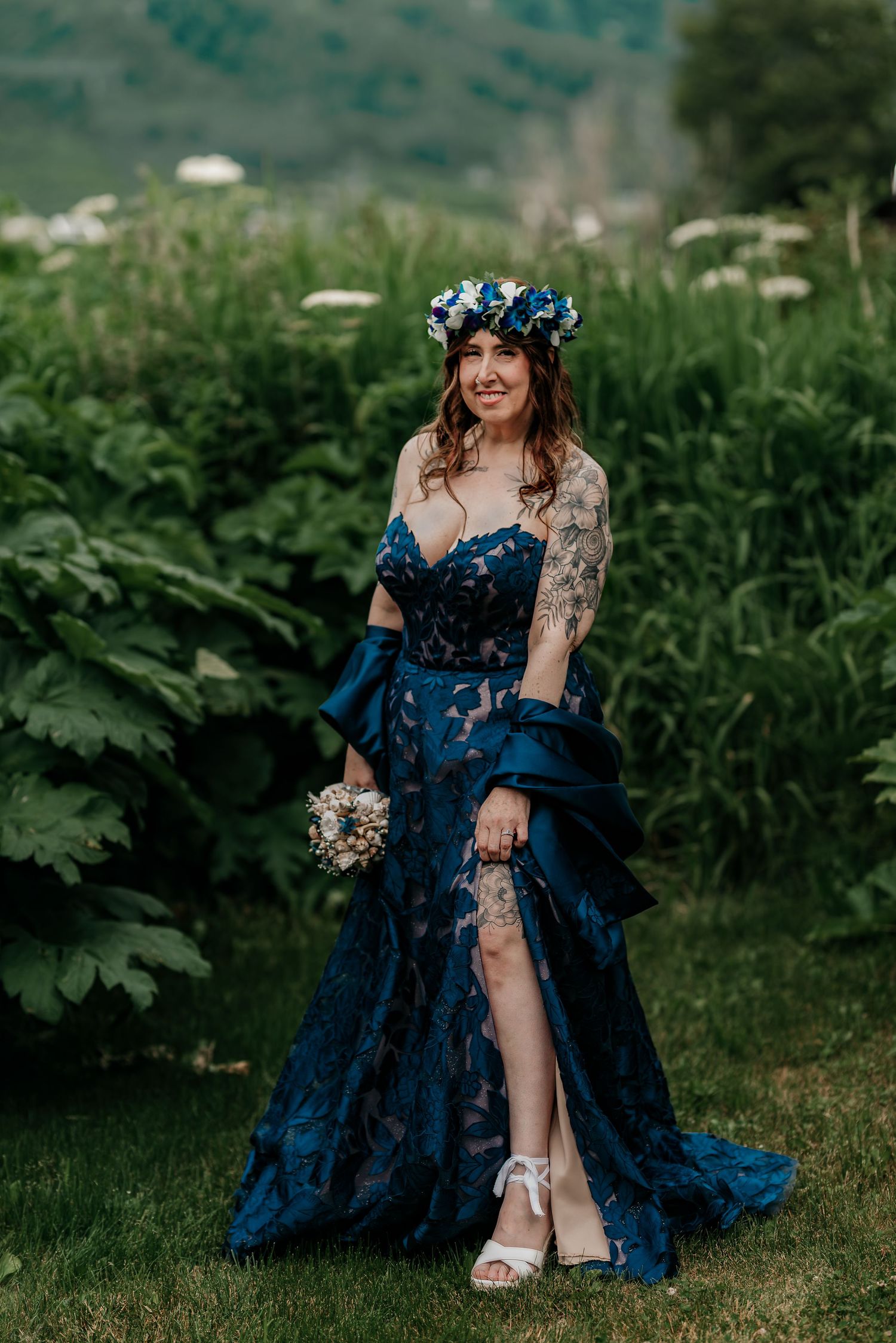 Bride in navy blue lace gown with floral crown holding bouquet in garden setting.