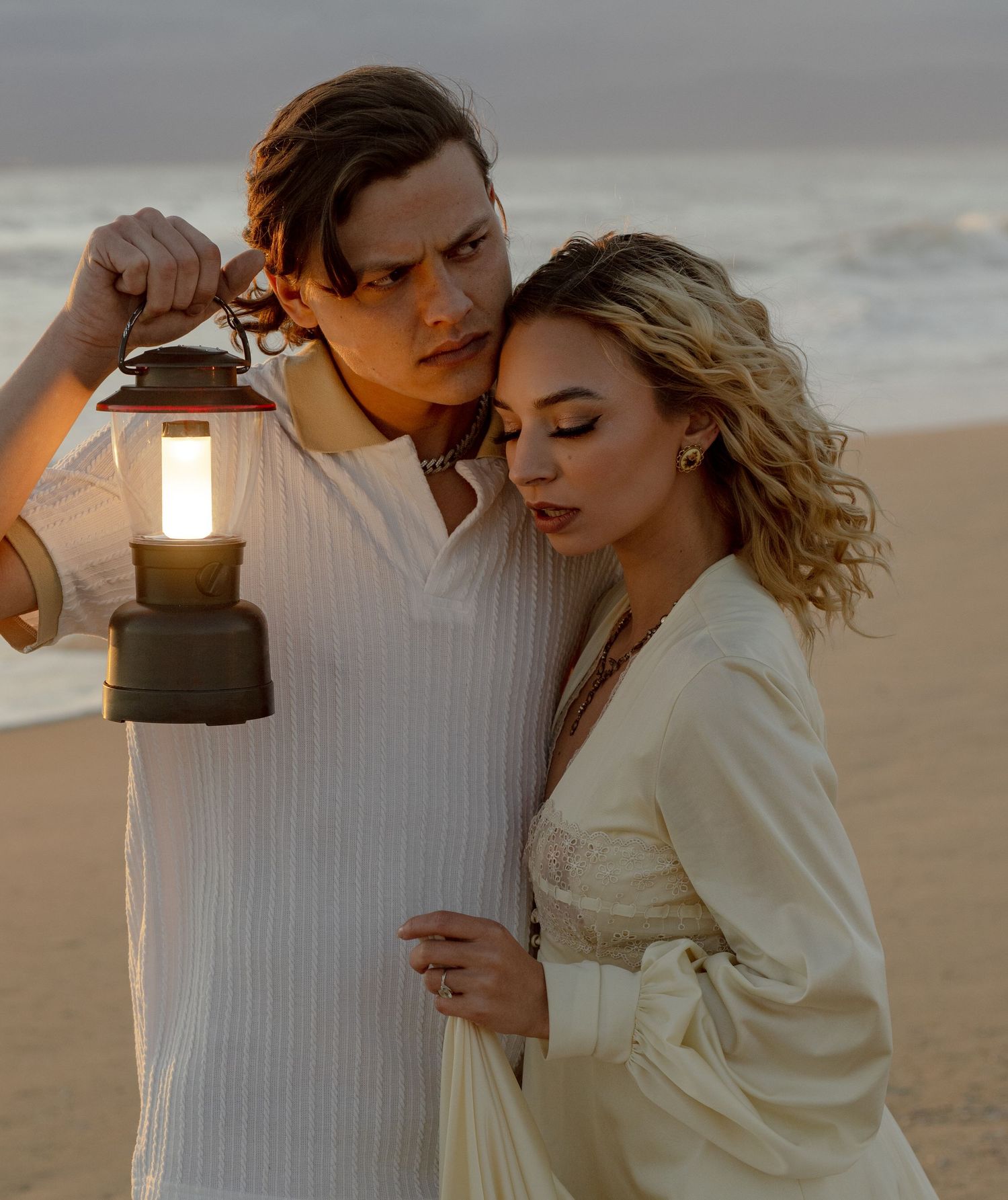 Romantic beach portrait with vintage lantern at golden hour.