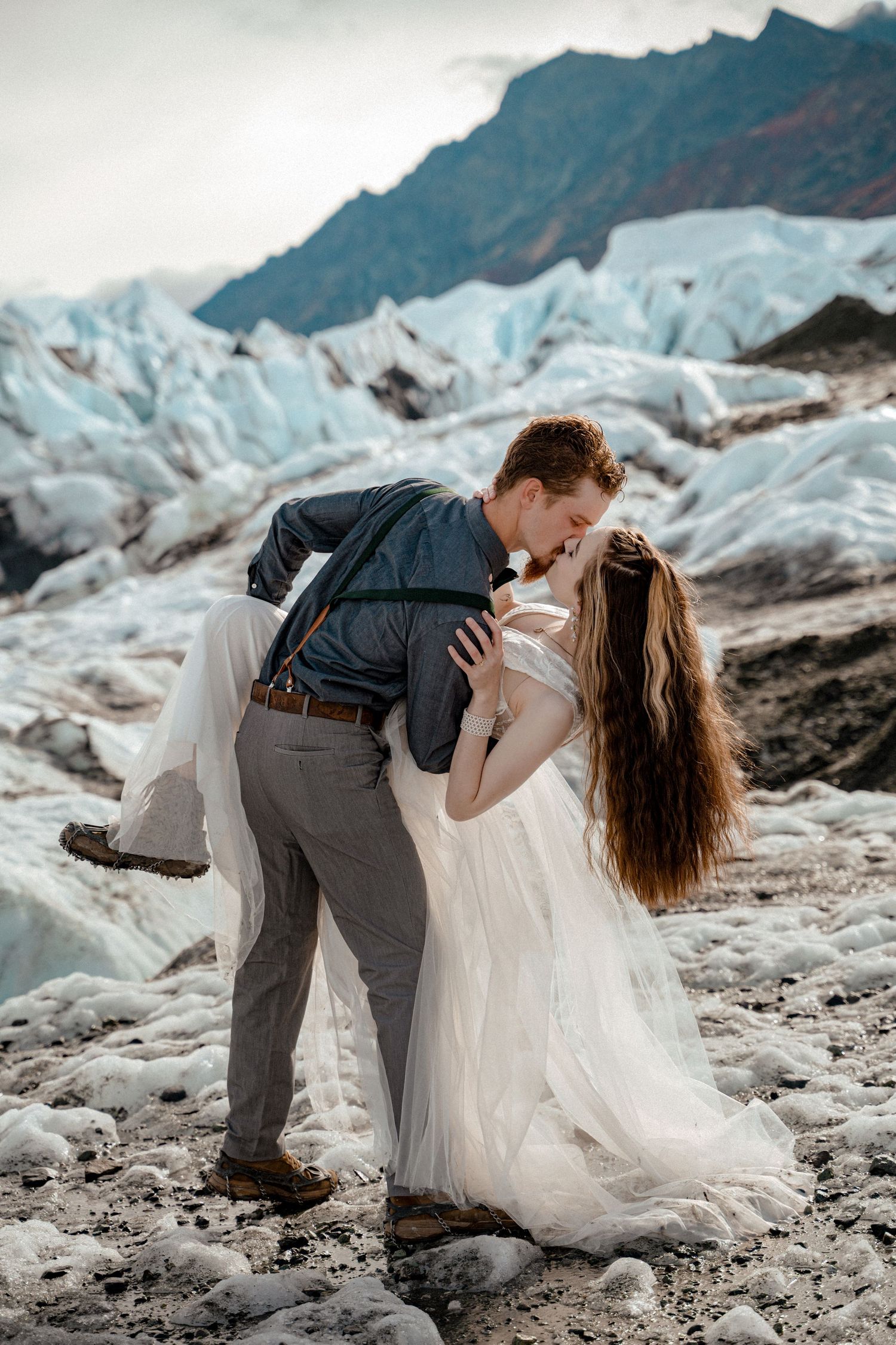 Bride and groom share a romantic kiss on a glacier, with the groom dipping his bride in a white wedding dress.