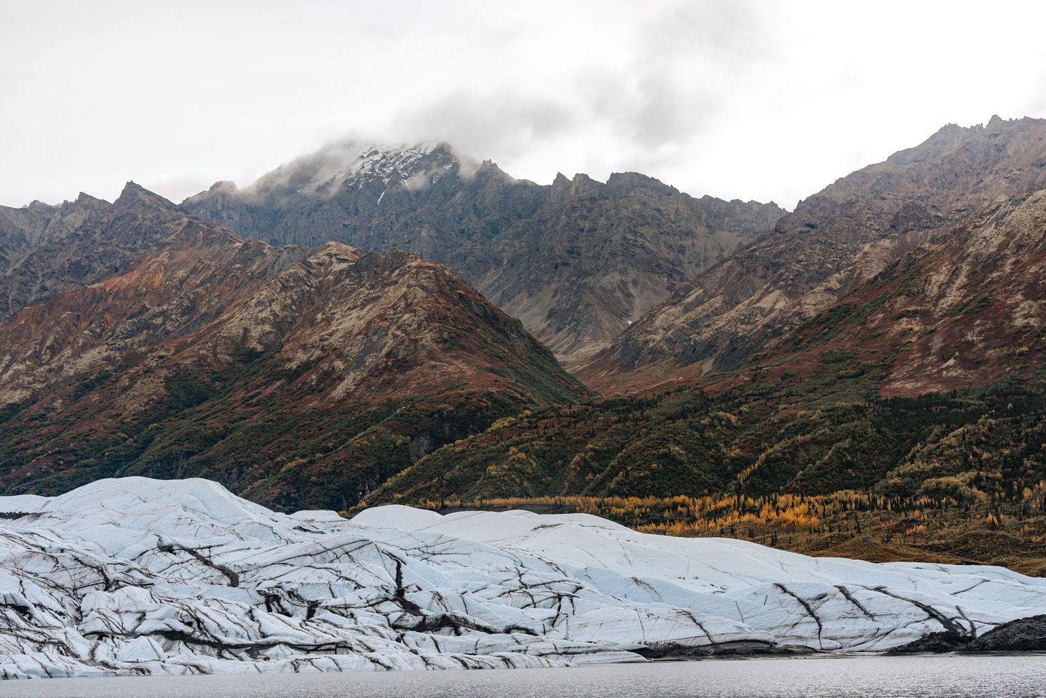 Dramatic aerial panorama of misty mountains and glacier fields in rugged wilderness terrain under cloudy skies.