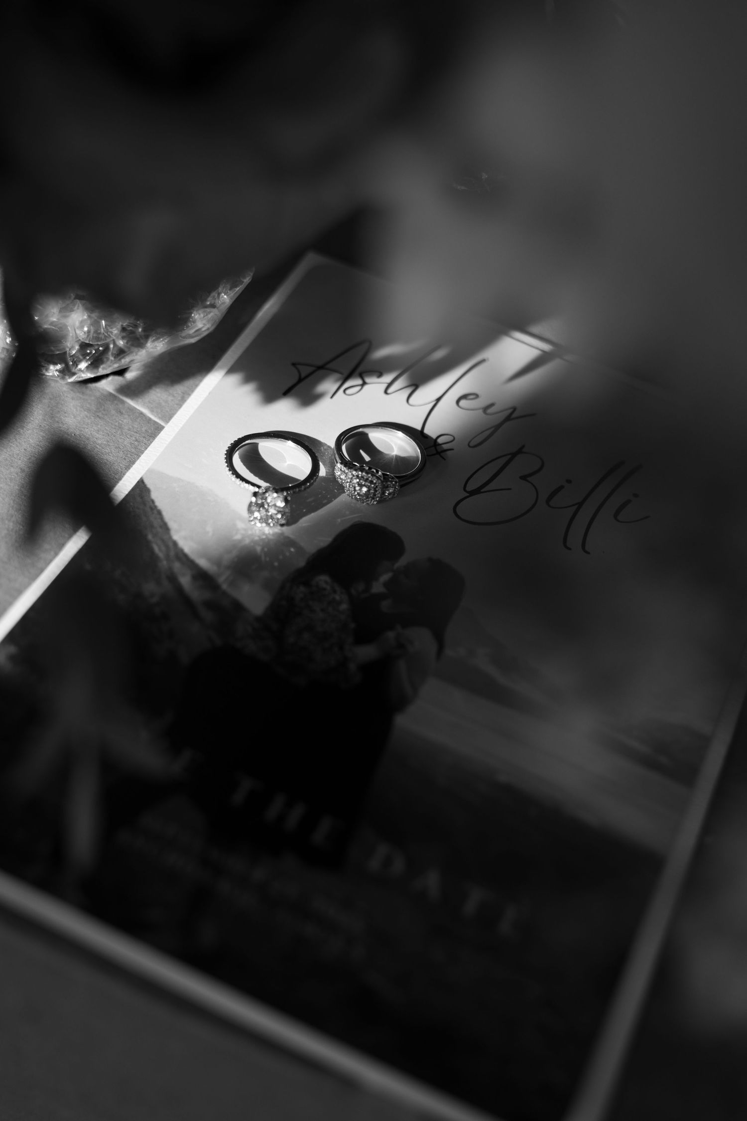 Black and white photo of wedding rings resting on a save the date card with elegant script lettering.
