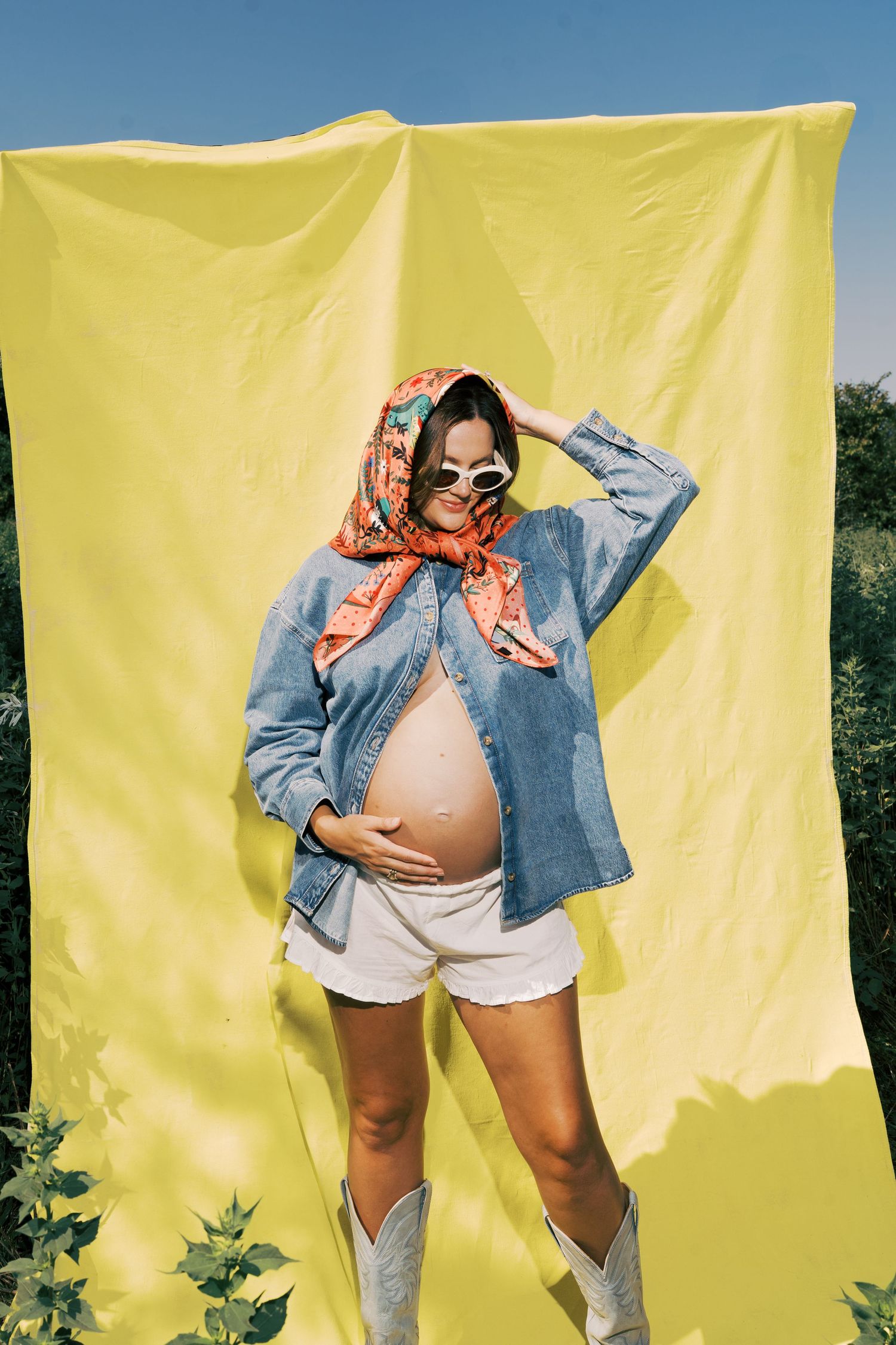 A pregnancy photo shoot features someone in denim against a bright yellow backdrop in multiple artistic poses.