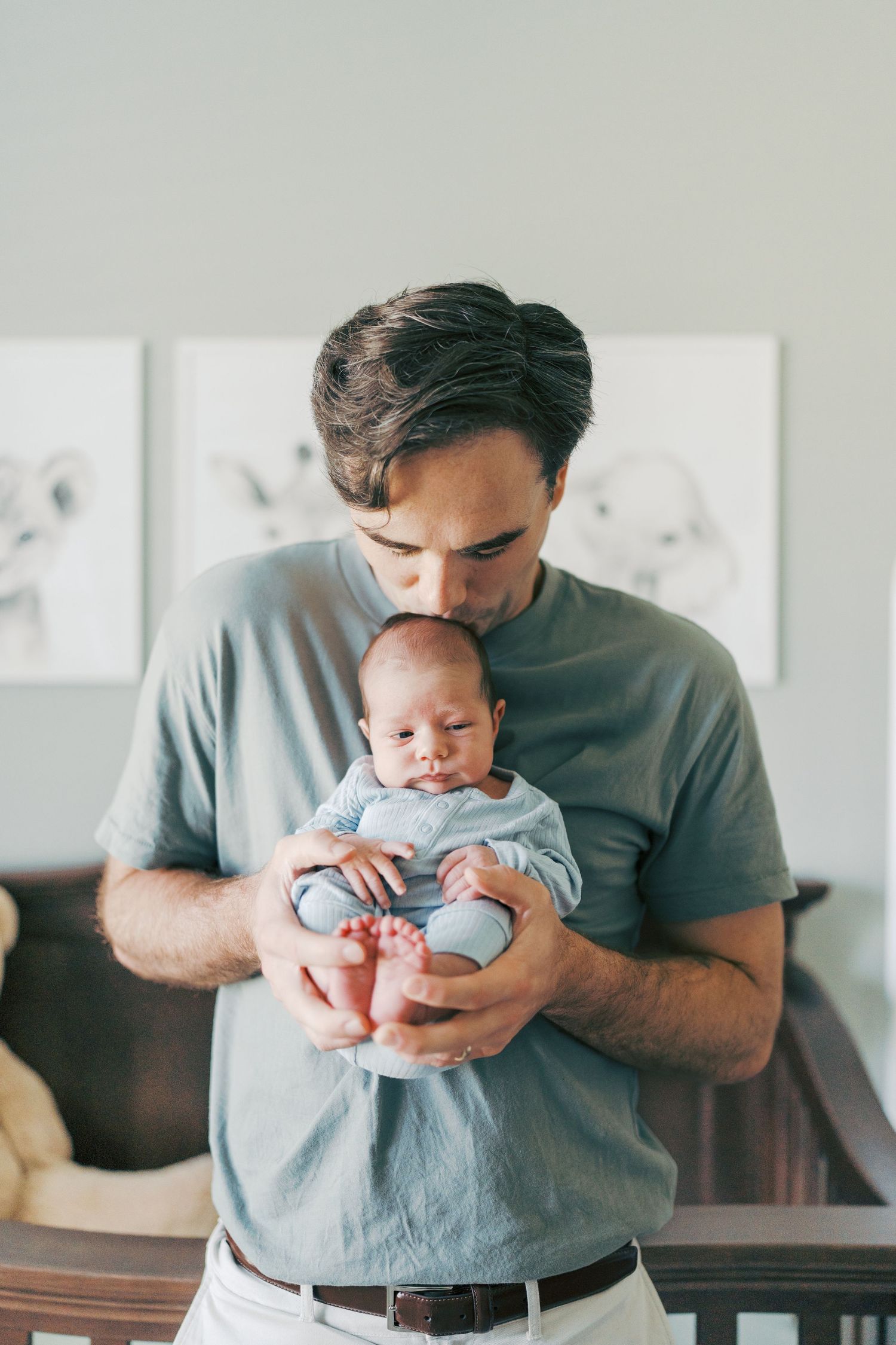A father tenderly kisses his newborn baby while cradling the infant in a cozy nursery room.