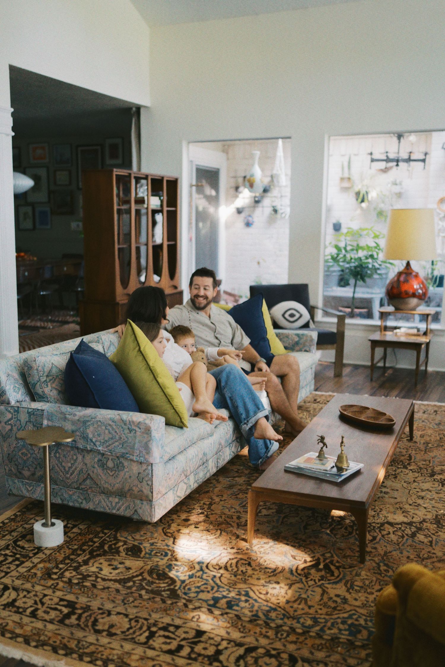 A couple relaxes on a patterned sofa with colorful pillows in a stylish mid-century modern living room with a coffee table.