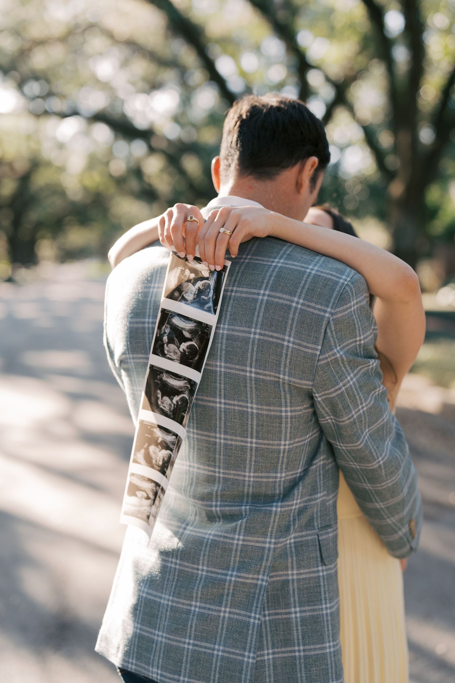 A couple embracing and holding a sonogram image in a park setting.