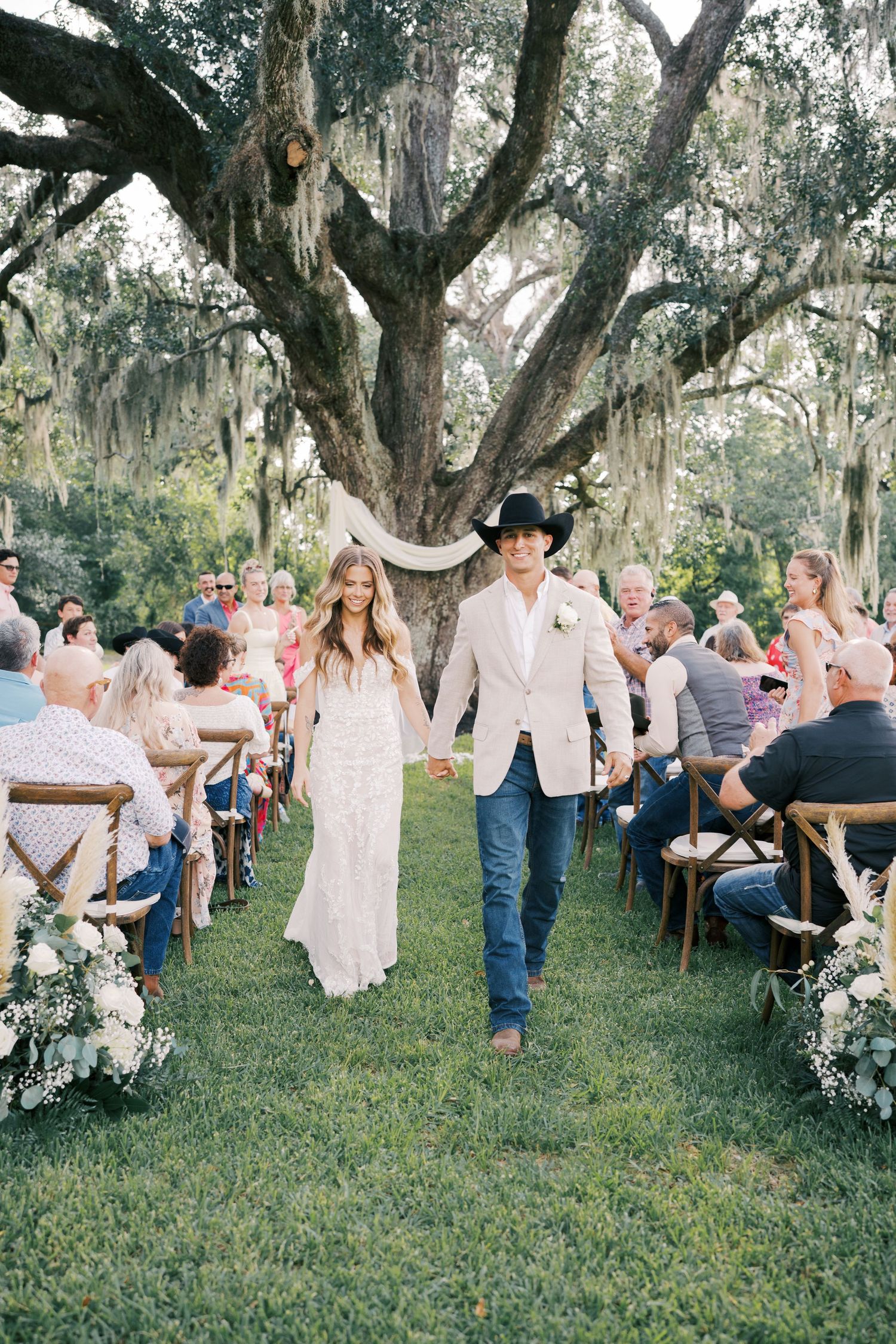 Rustic outdoor wedding reception under oak trees with string lights.
