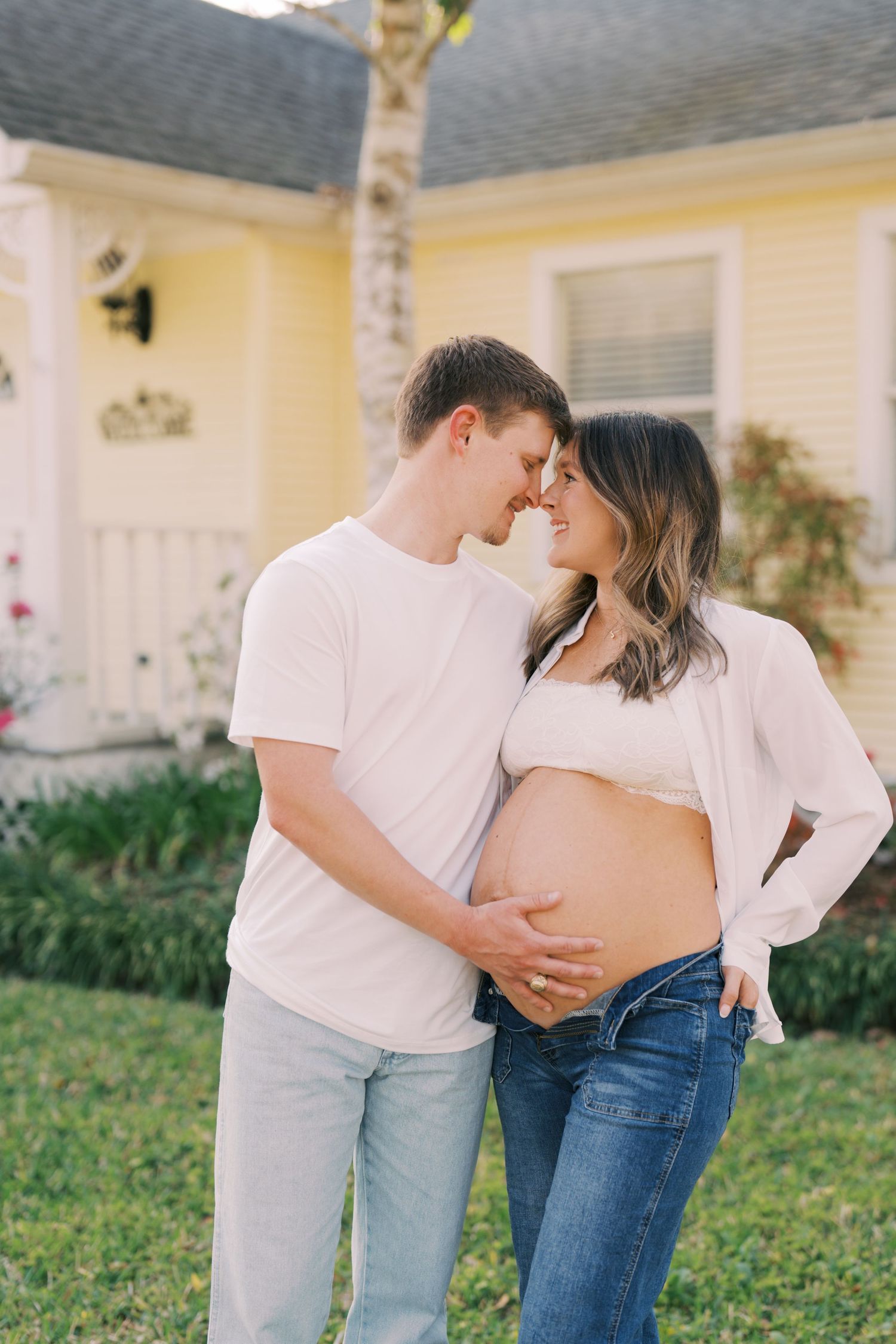 A couple in white shirts shares an intimate moment outdoors while celebrating an expected baby.