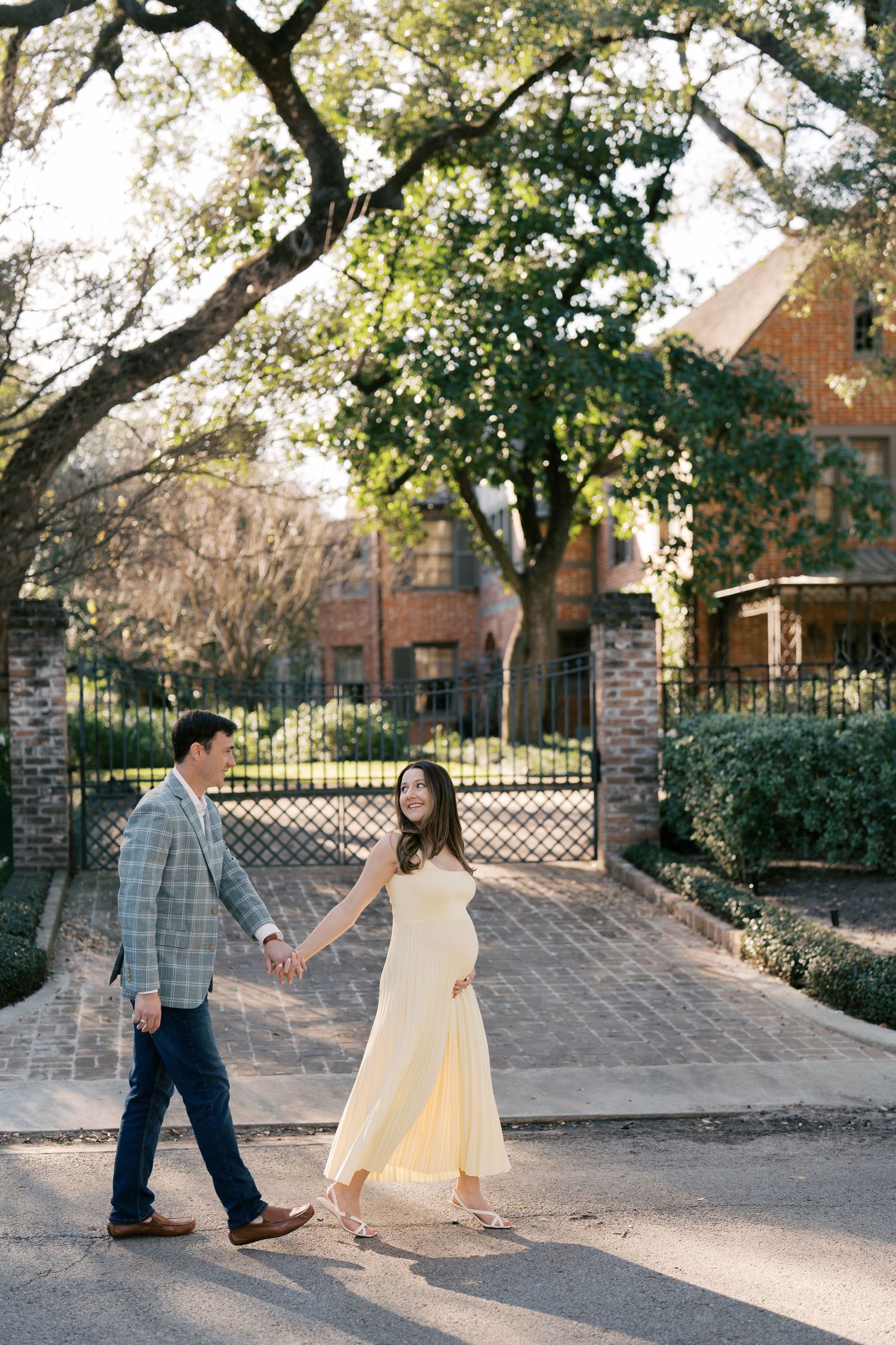 A couple holding hands and walking together on a brick path surrounded by trees and foliage.