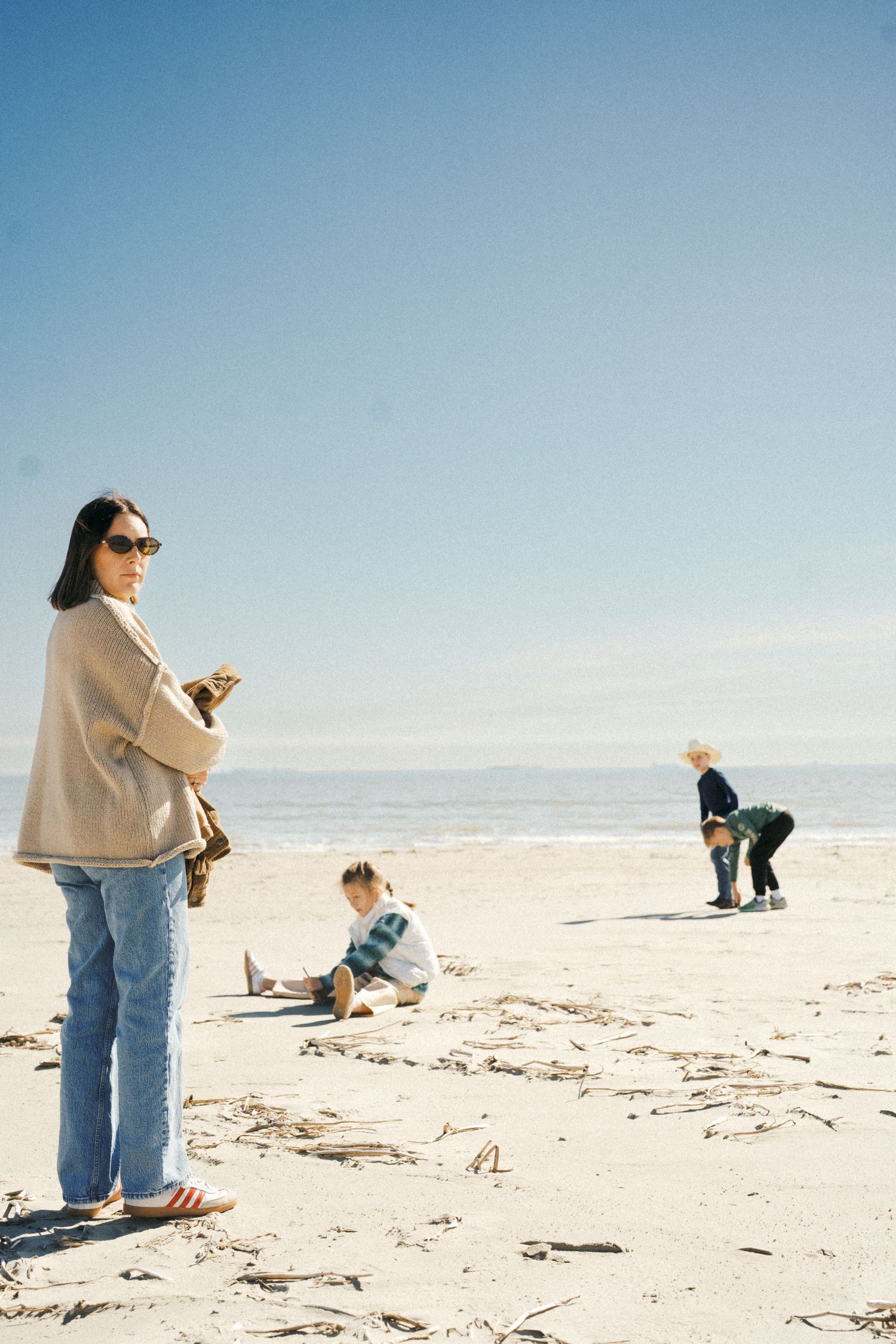 A sequence of people searching and collecting items on a sunny beach against a bright blue sky.