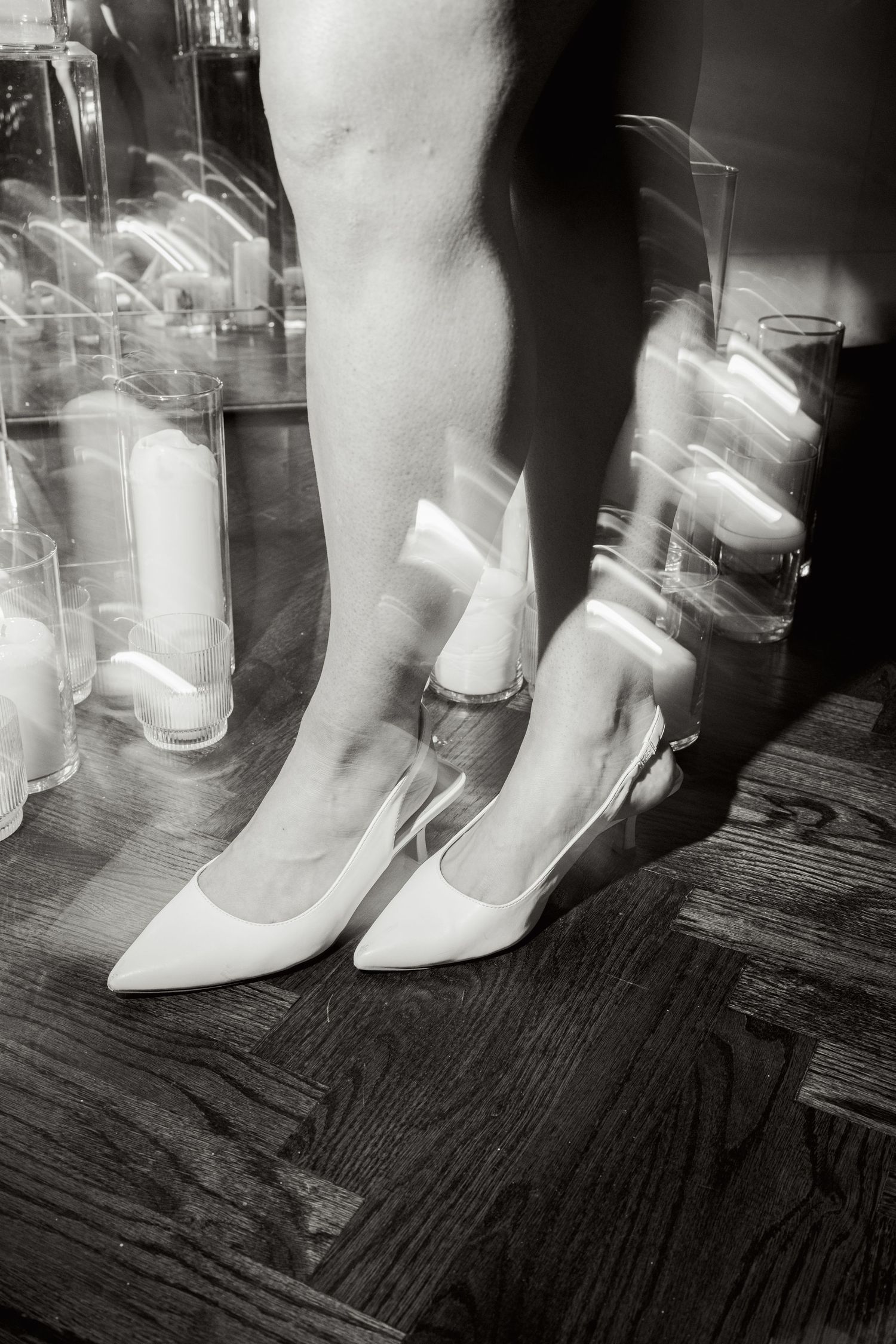 An artistic black and white photo of white bridal shoes on a hardwood floor.