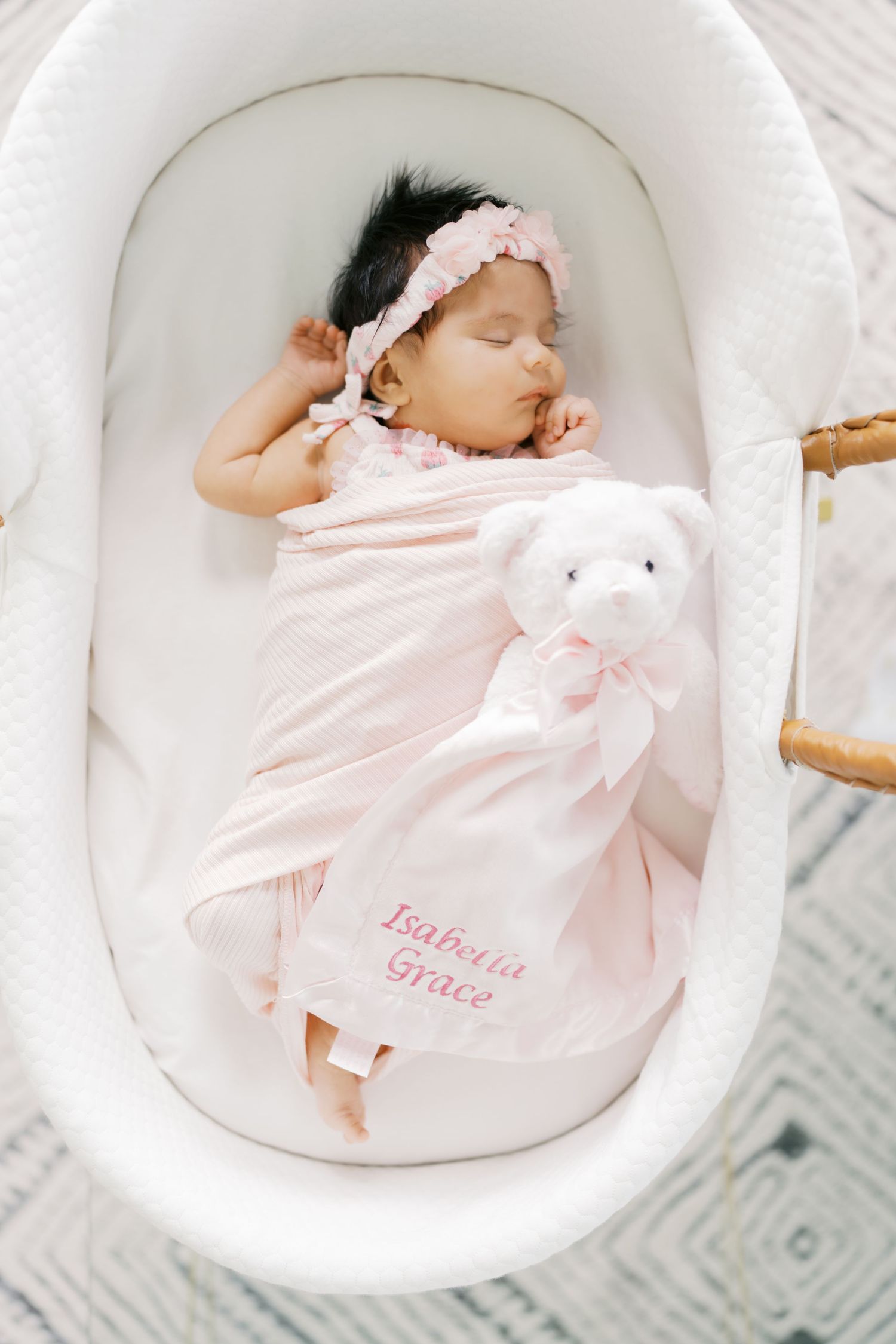Newborn baby girl sleeping in white bassinet with pink blanket, teddy bear, and headband, named Isabella Grace.