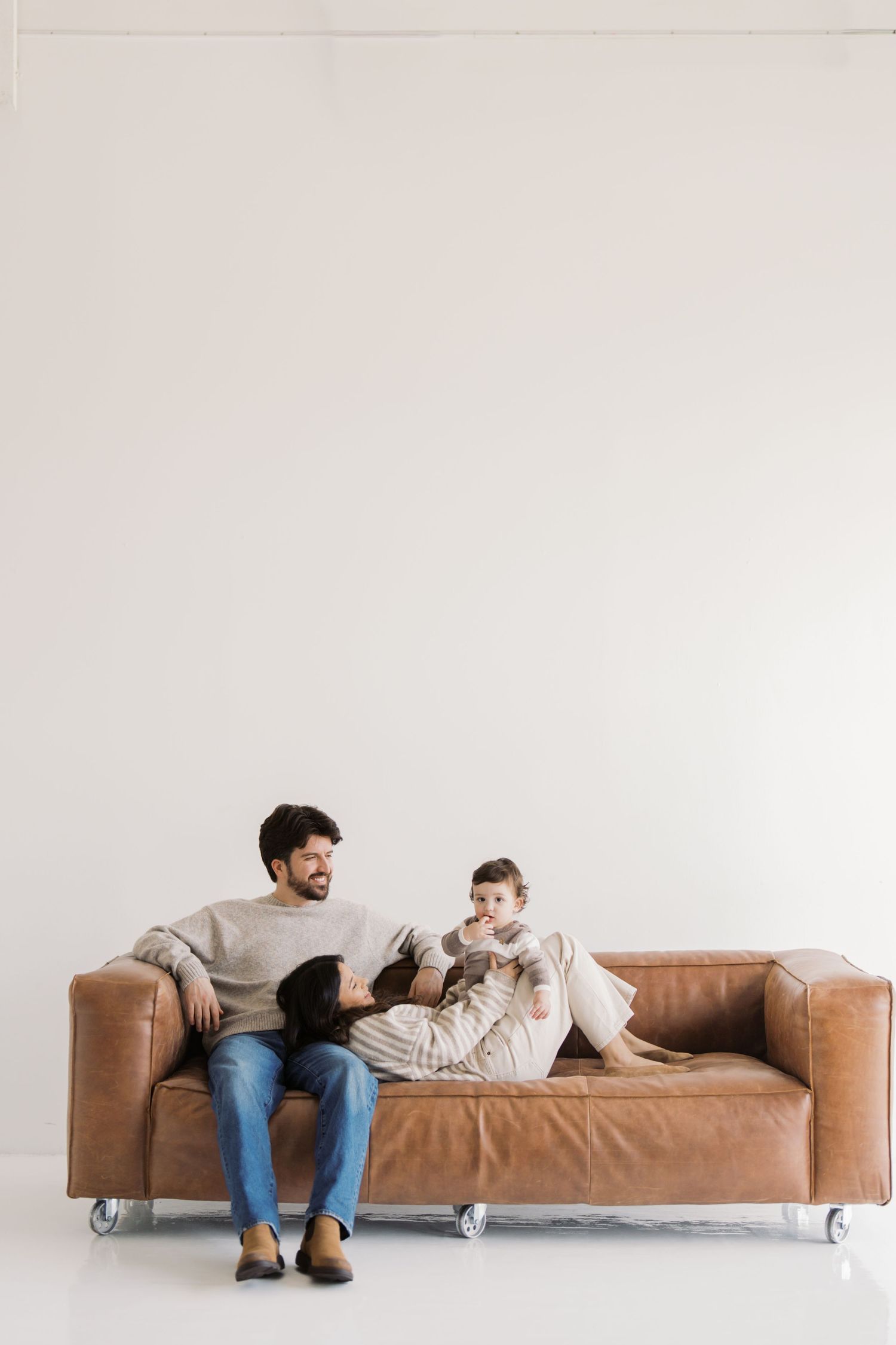 A man and a young child sitting together on a leather sofa against a plain white wall.